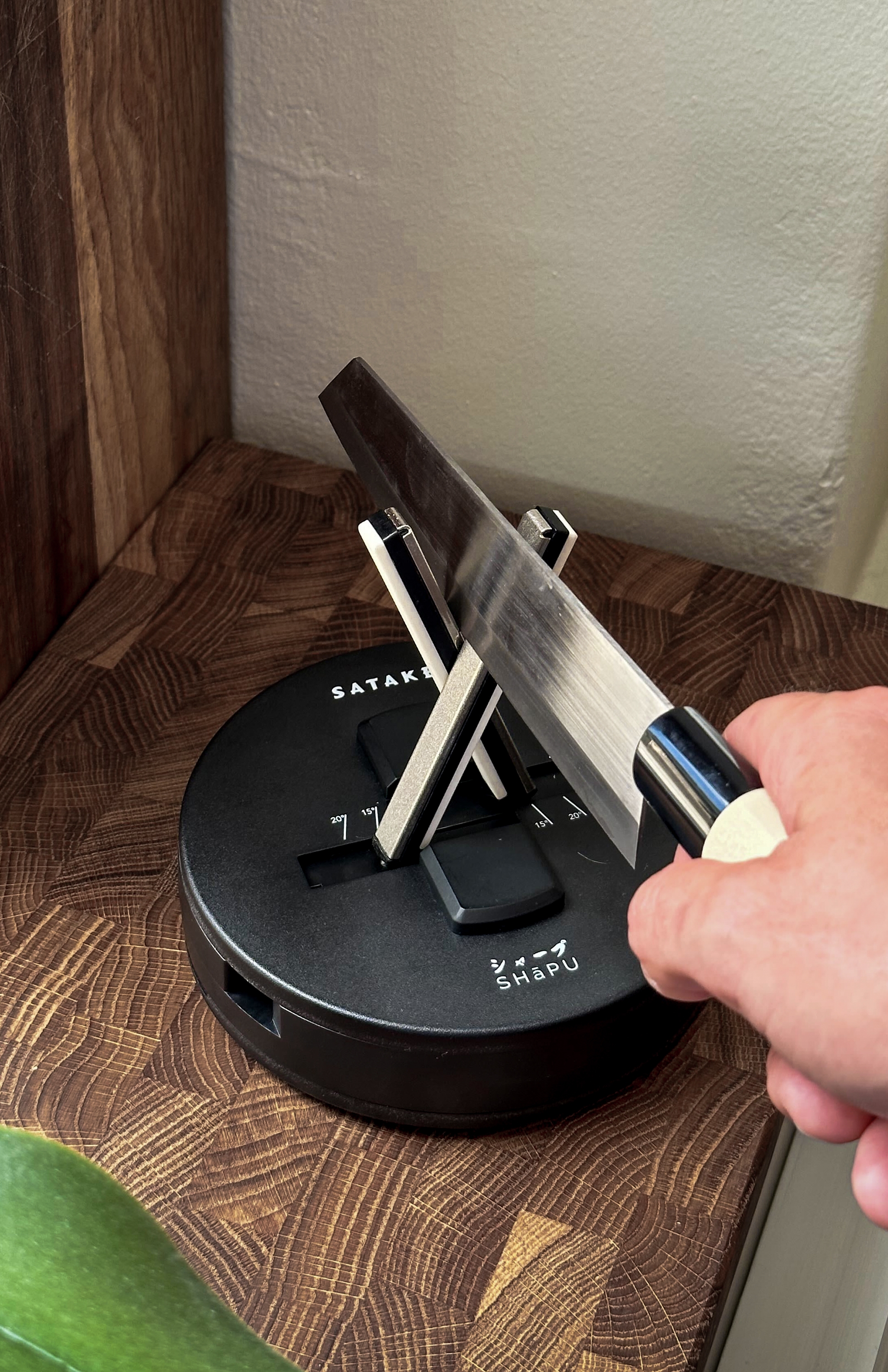 En persons hand styr en kniv in i en svart knivslipare som vilar på ett slaktblock av trä.