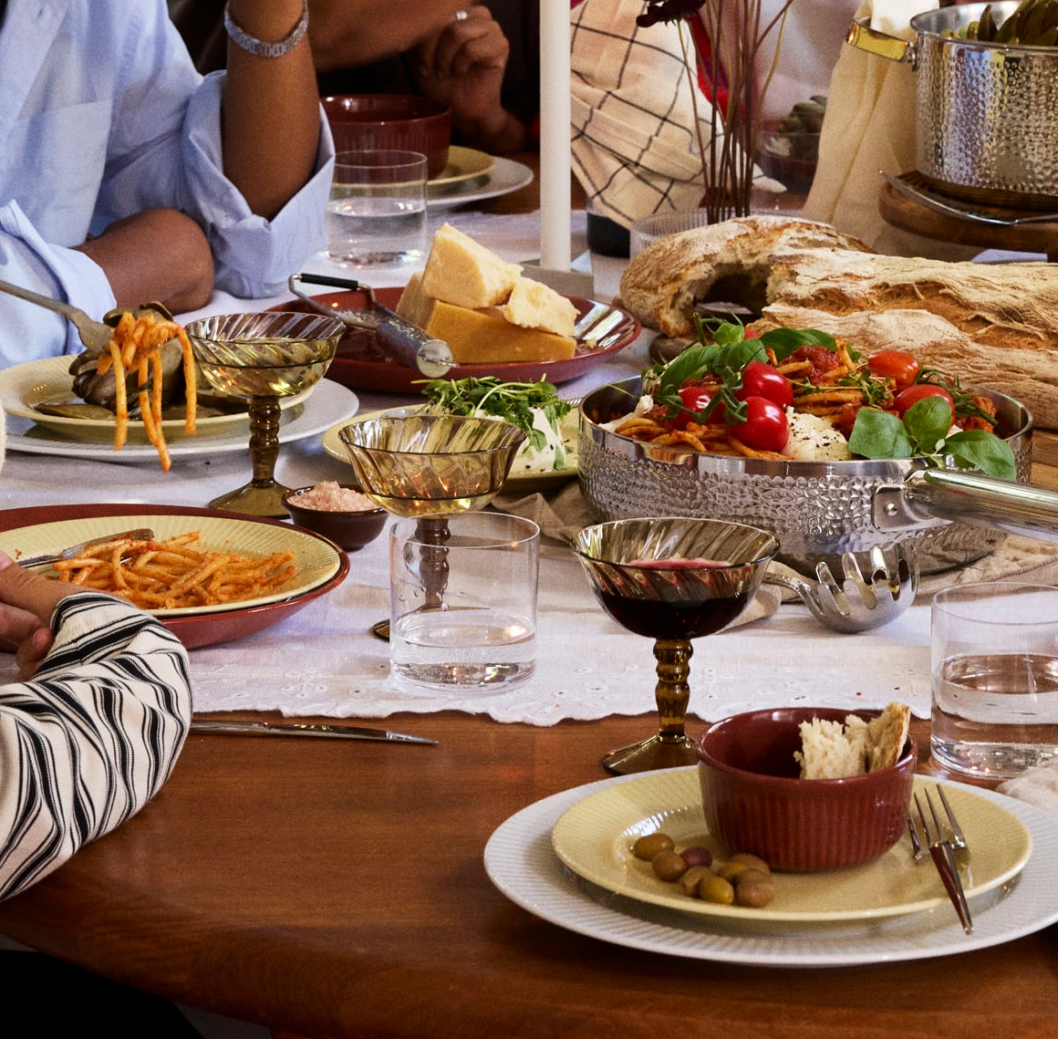 Venner og familie nyter et hyggelig middagsselskap med pasta, brød og vin rundt et dekket bord.
