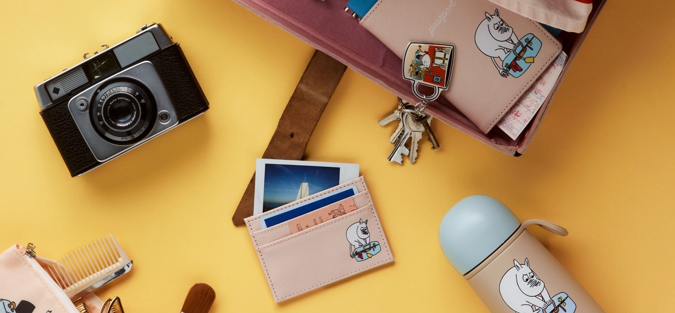 A vintage camera and an open pink container holding a passport, keys, and a pen, all on a yellow background.