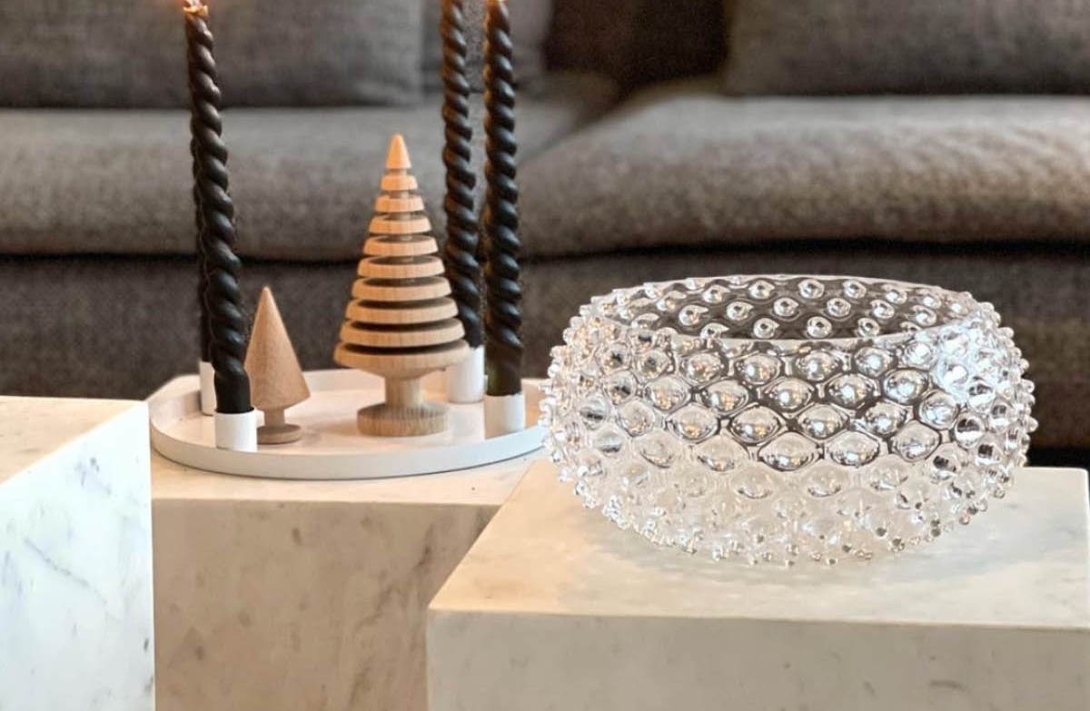 Svarta spiralformade ljus, dekorativa trägranar och en skål i bubbligt glas på marmorbord framför en grå soffa.