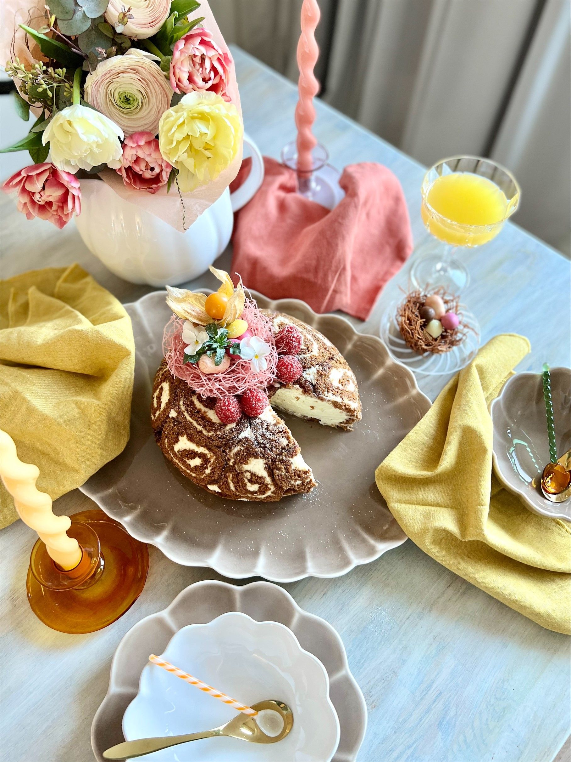 Ett festligt vårbord med en chokladrulltårta med virvelmönster, hallon och påskäggsdekorationer
