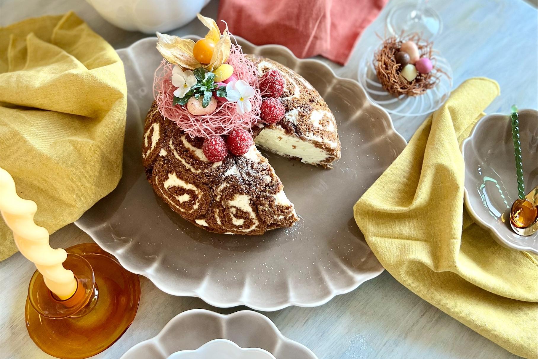 Ett festligt vårbord med en chokladrulltårta med virvelmönster, hallon och påskäggsdekorationer