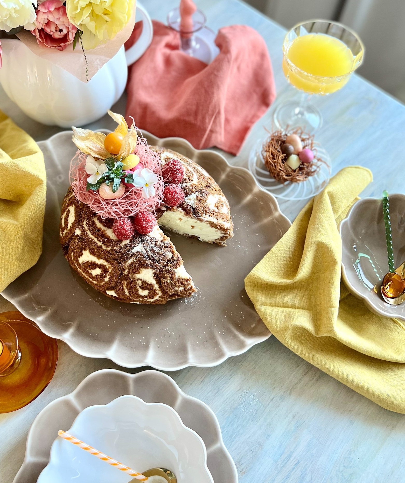 Ett festligt vårbord med en chokladrulltårta med virvelmönster, hallon och påskäggsdekorationer