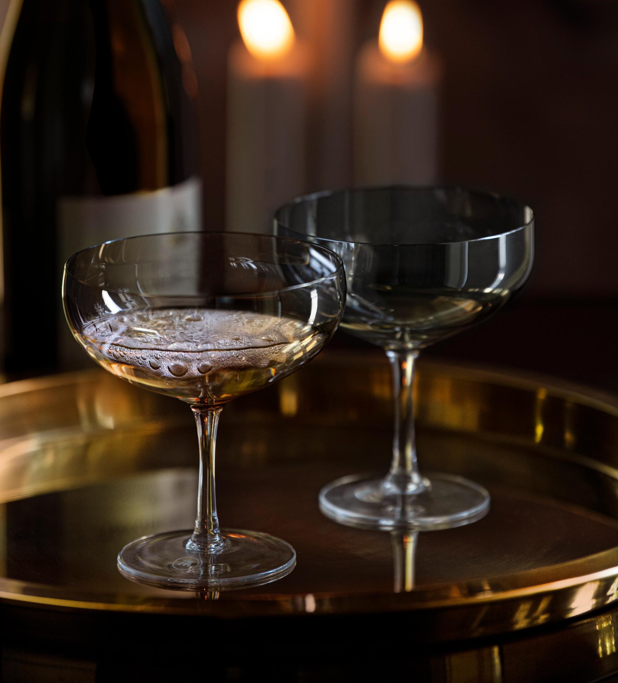 Två champagneglas och en flaska på en guldfärgad bricka framför tre tända ljus.