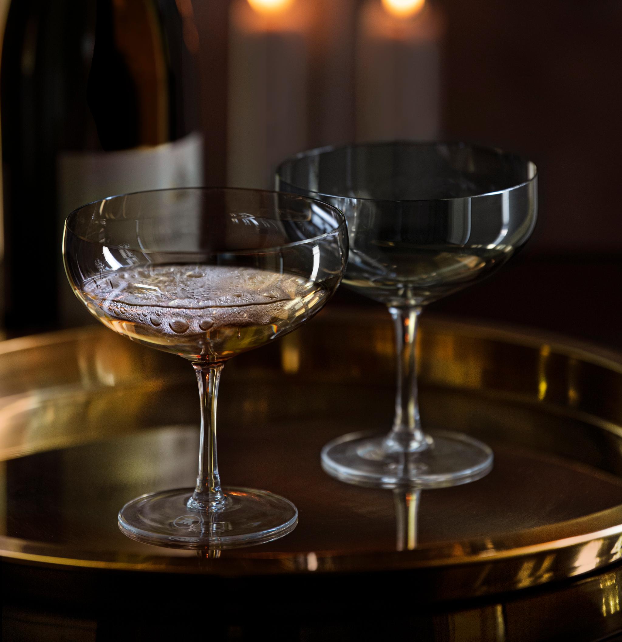 To champagneglass, en champagneflaske og tente stearinlys på et elegant gullbrett.