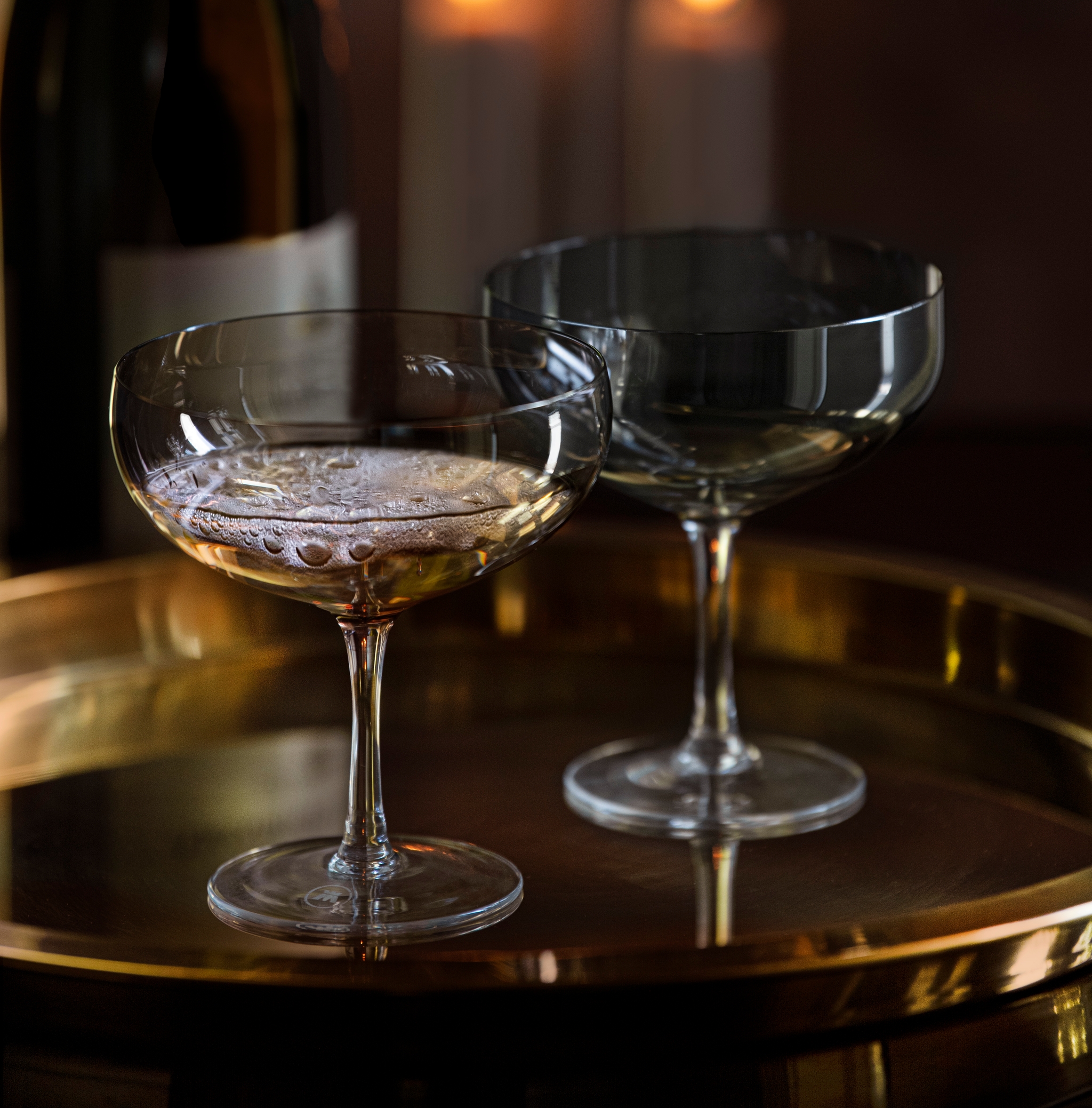 To champagneglass, en champagneflaske og tente stearinlys på et elegant gullbrett.