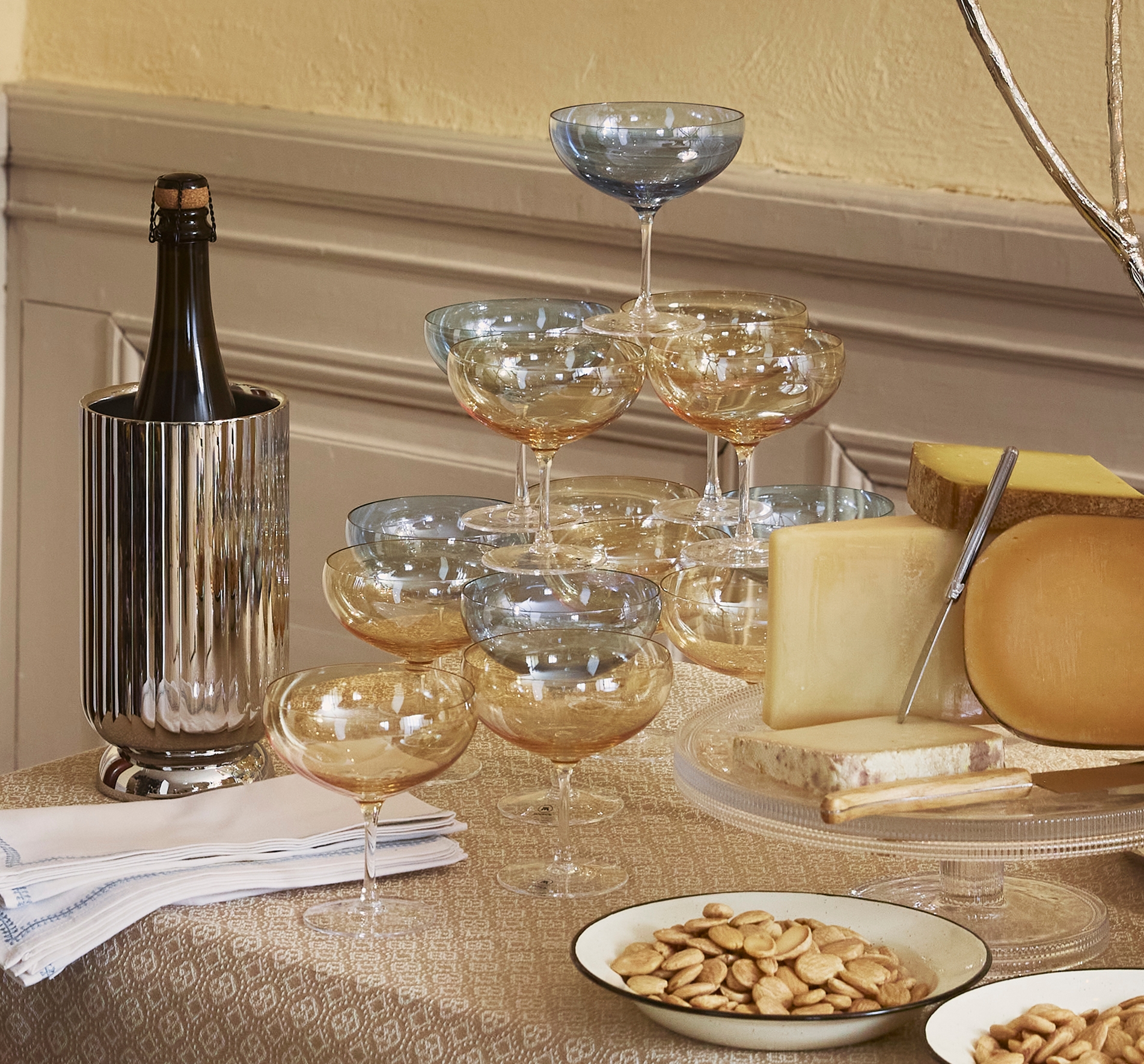 Elegant buffetbord med brød, ost, druer, nøtter, champagneglass og tente lys i et varmt, klassisk interiør.