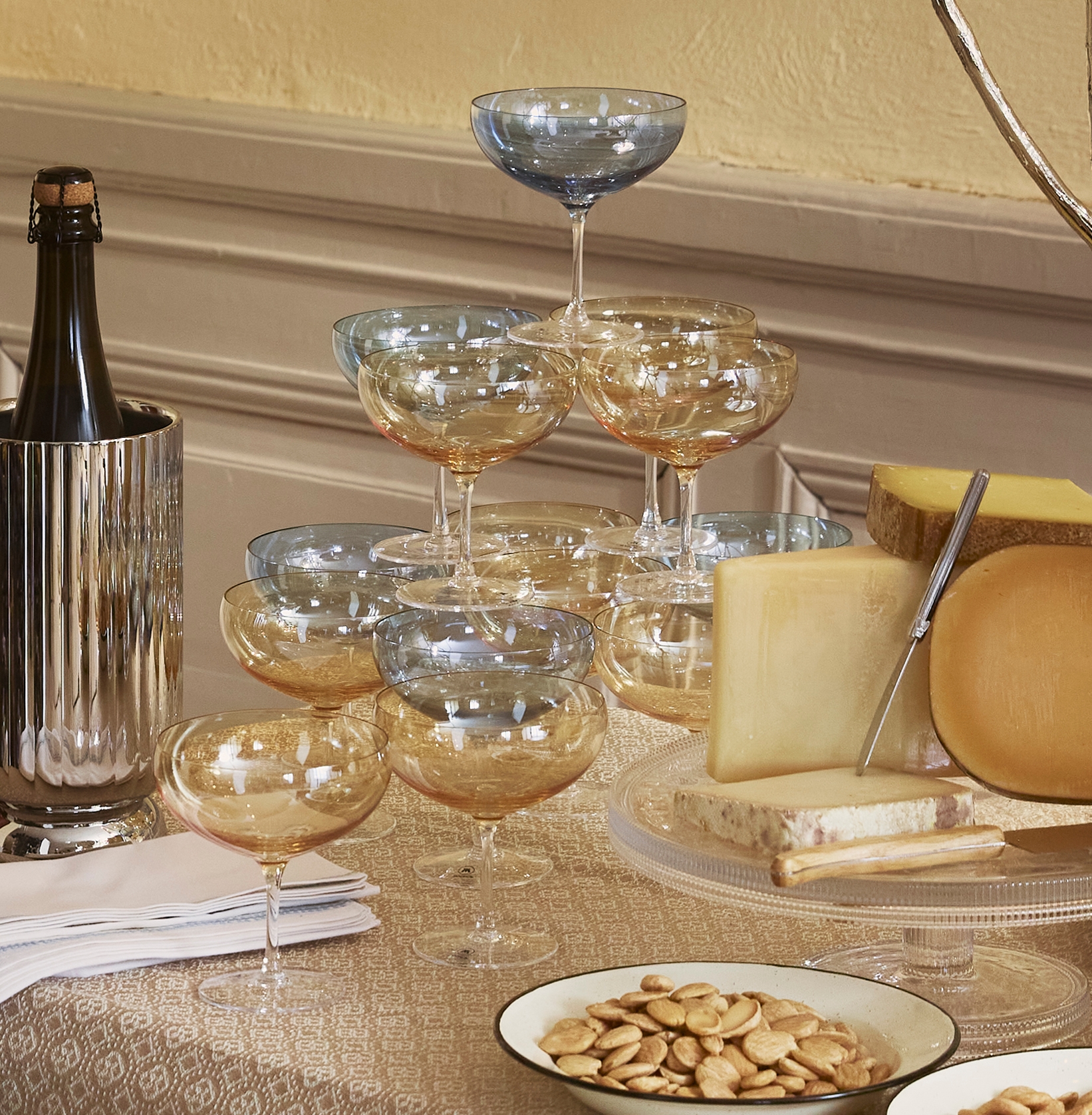Elegant festbord med brød, ost, druer, nøtter, champagneglass og tente lys i et klassisk, varmt innredet rom.