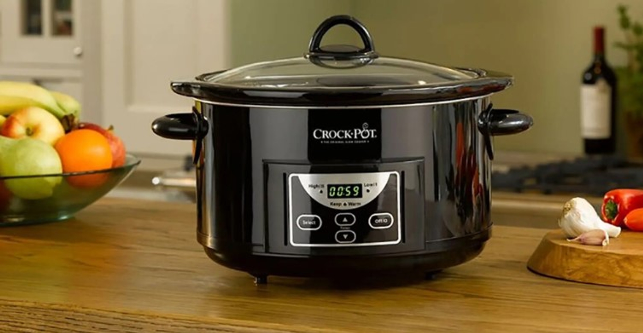 Slow cooker med timer svart på trebord, fruktskål i bakgrunnen