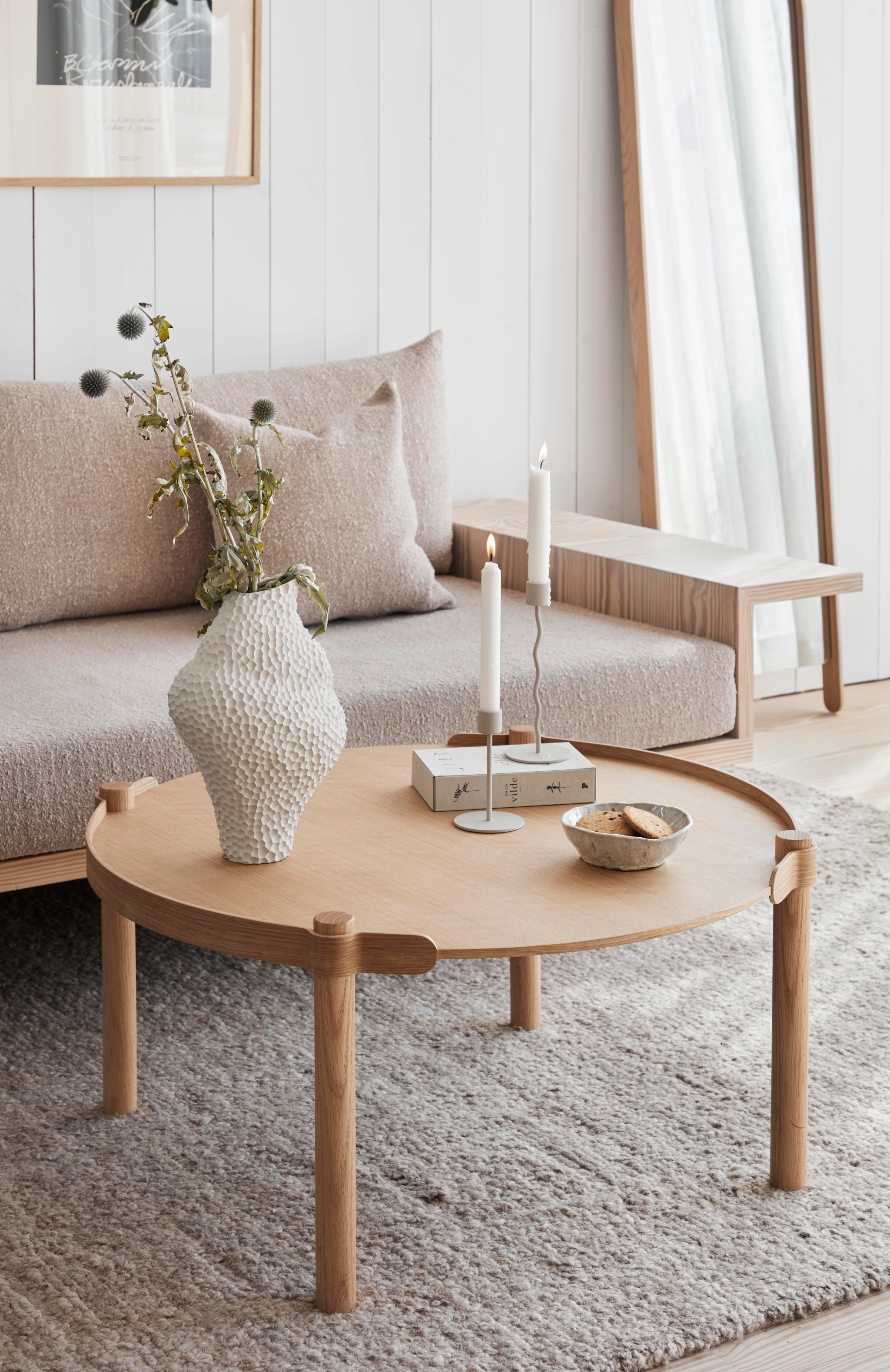 Vardagsrum med en beige soffa, ek träbord, en vit vas och guldiga ljusstakar