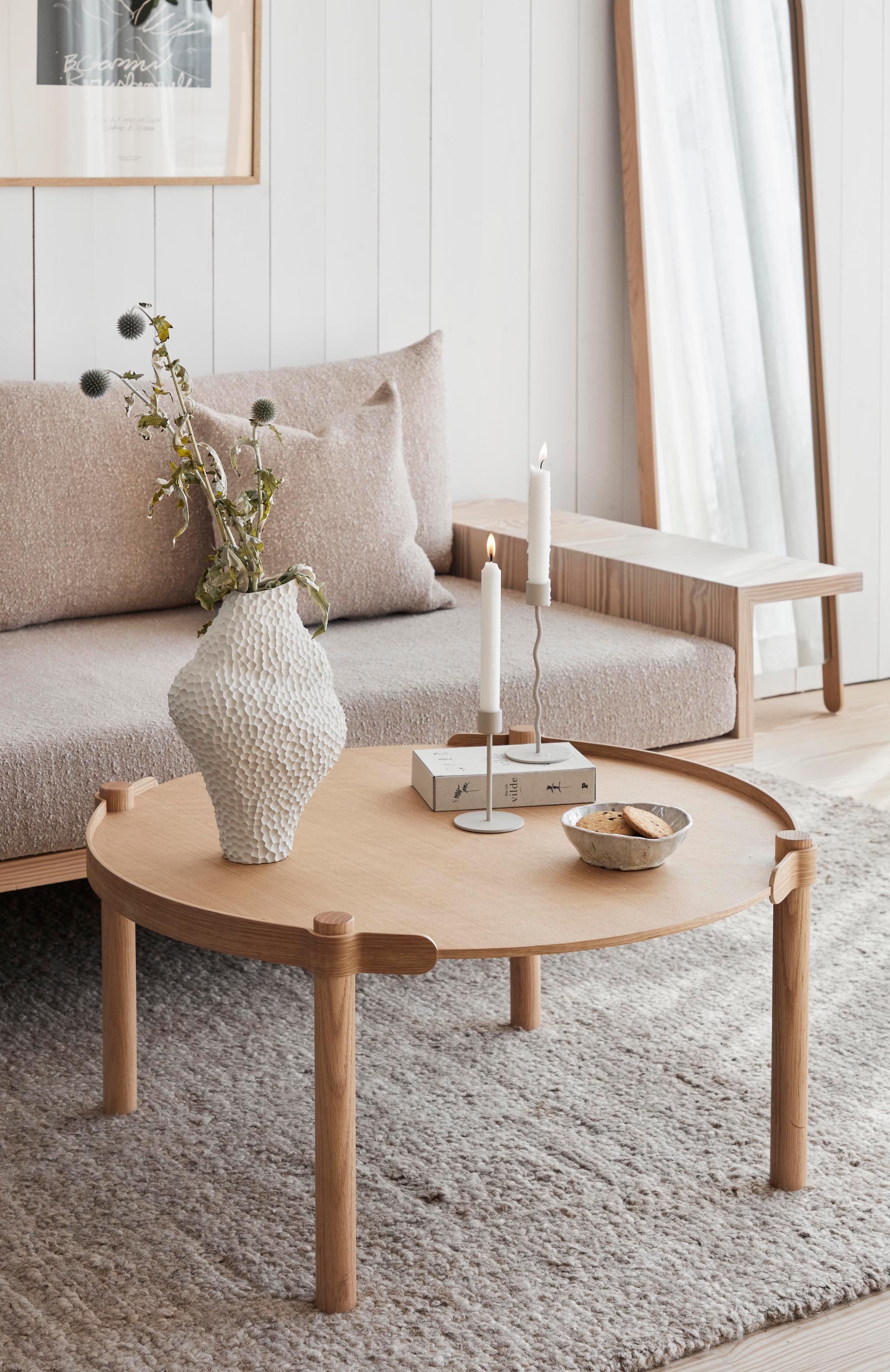 Vardagsrum med en beige soffa, ek träbord, en vit vas och guldiga ljusstakar