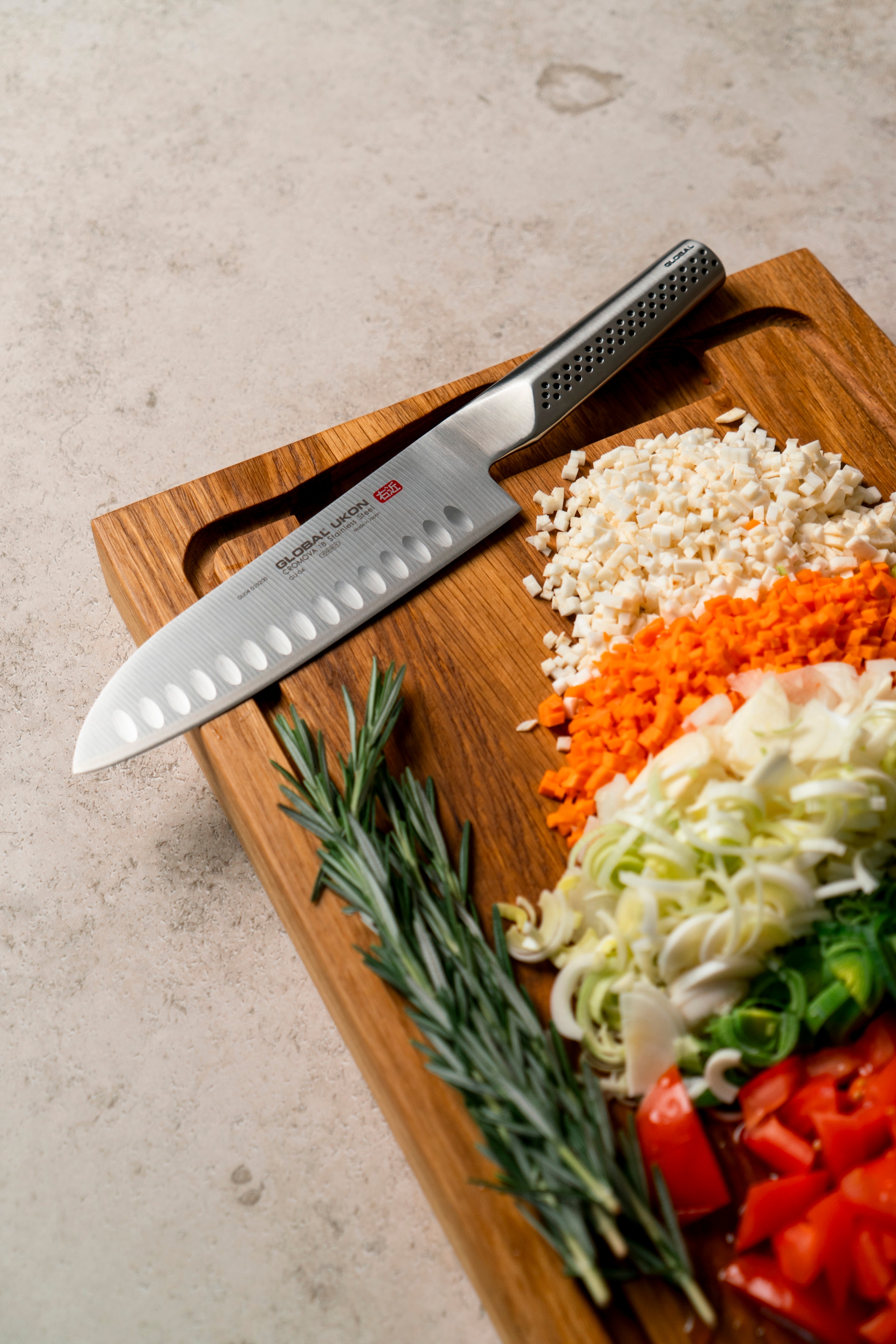 Kockkniv på en skärbräda med finhackade grönsaker och färsk rosmarin.