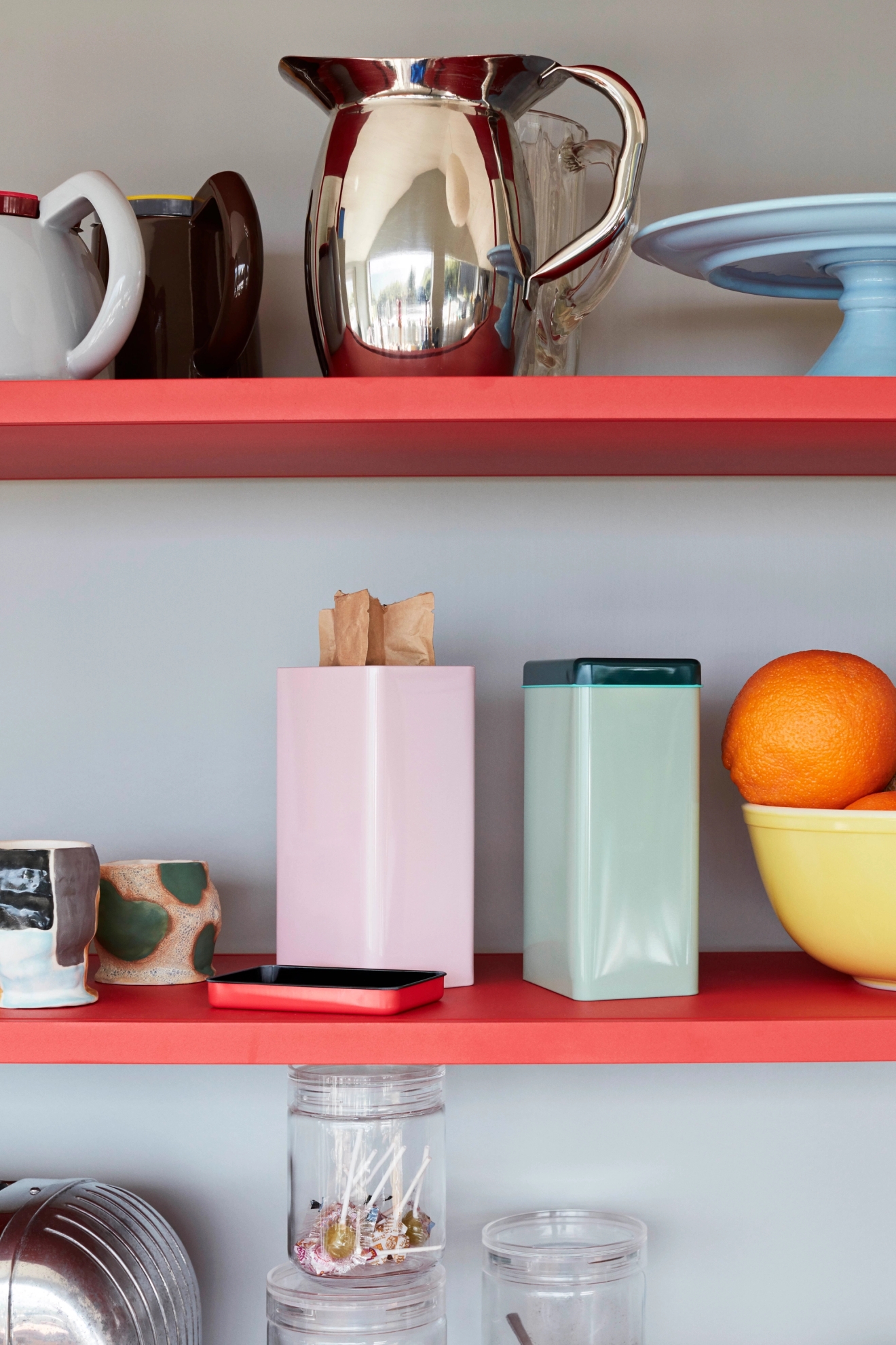 Askar och burkar i rosa och grön plåt på röd hylla 
