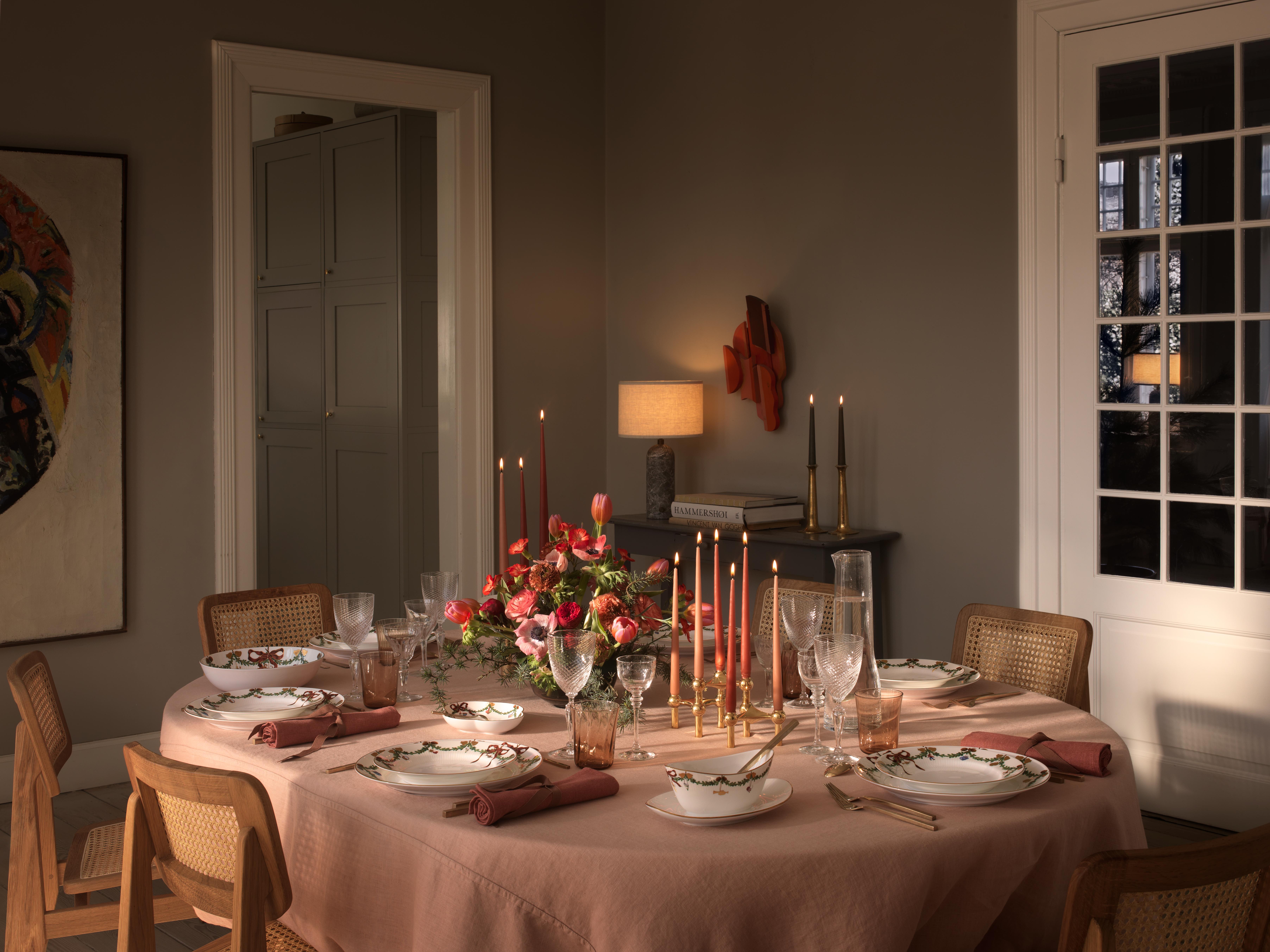 Ett dukat bord för en middagsbjudning med julporslin, ljus och blommor.