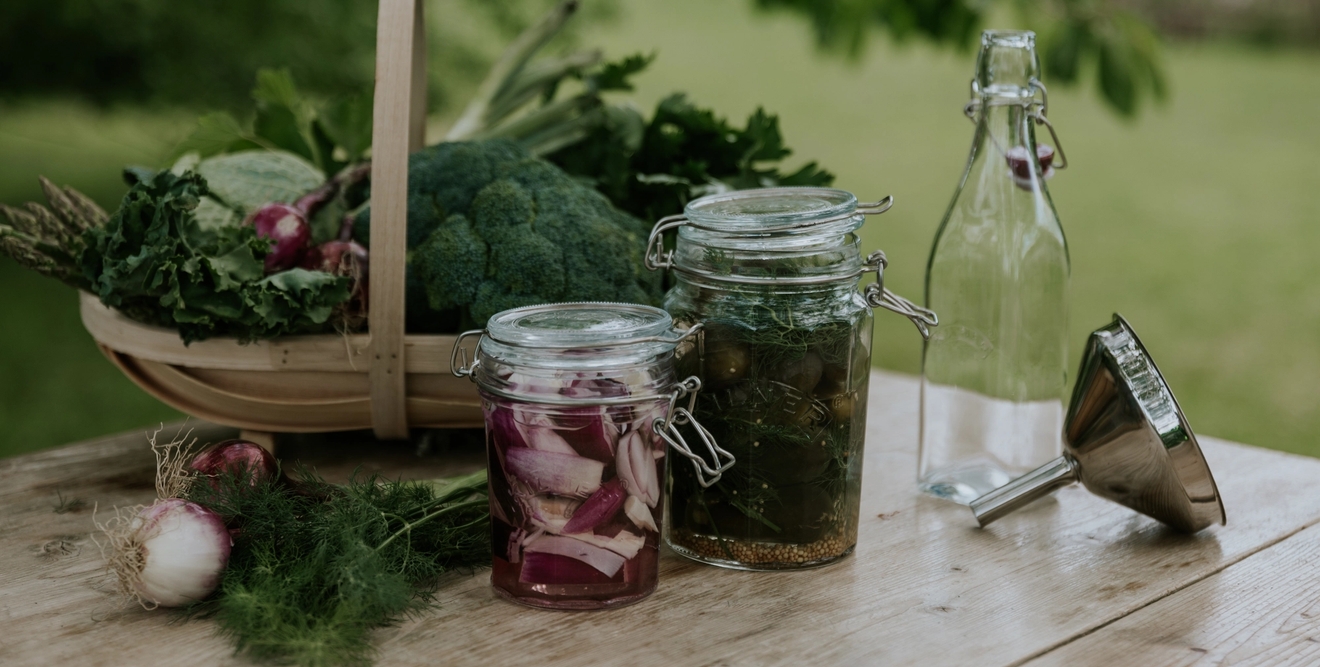 Fermenterte grønnsaker på glass ved siden av en kurv full av grønnkål