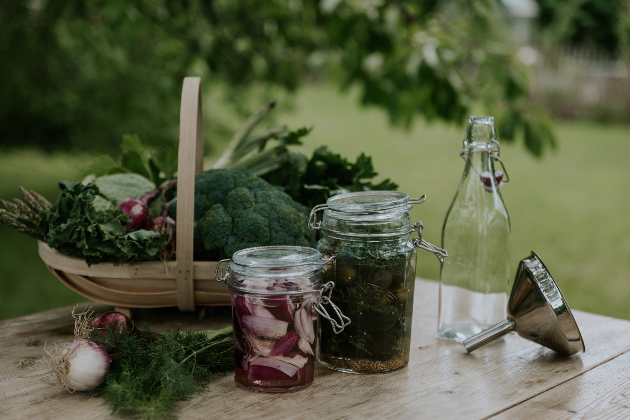 Fermenterte grønnsaker på glass ved siden av en kurv full av grønnkål