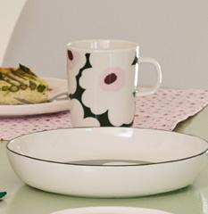 Ruokapöytä, jossa on vihreäraidallinen maljakko, jossa on vihreitä kasveja, quiche-viipale, kukkakuvioinen muki ja värikkäitä lasiesineitä.