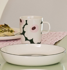 Ruokapöytä, jossa on vihreäraidallinen maljakko, jossa on vihreitä kasveja, quiche-viipale, kukkakuvioinen muki ja värikkäitä lasiesineitä.