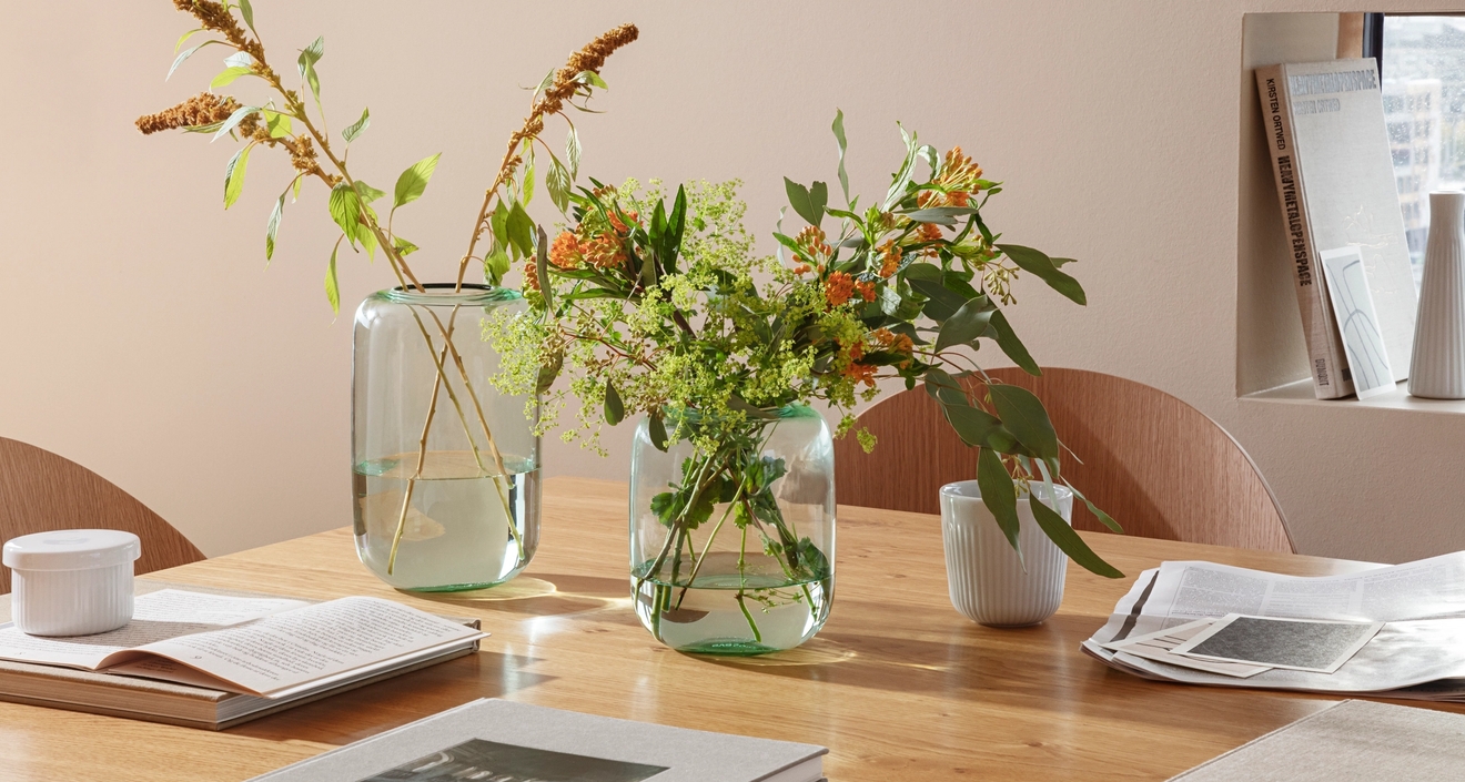 eva solo maljakko valmistettu lasista sävyssä vihreä ruokapöydällä kukkien kirjojen ja lehtien kera