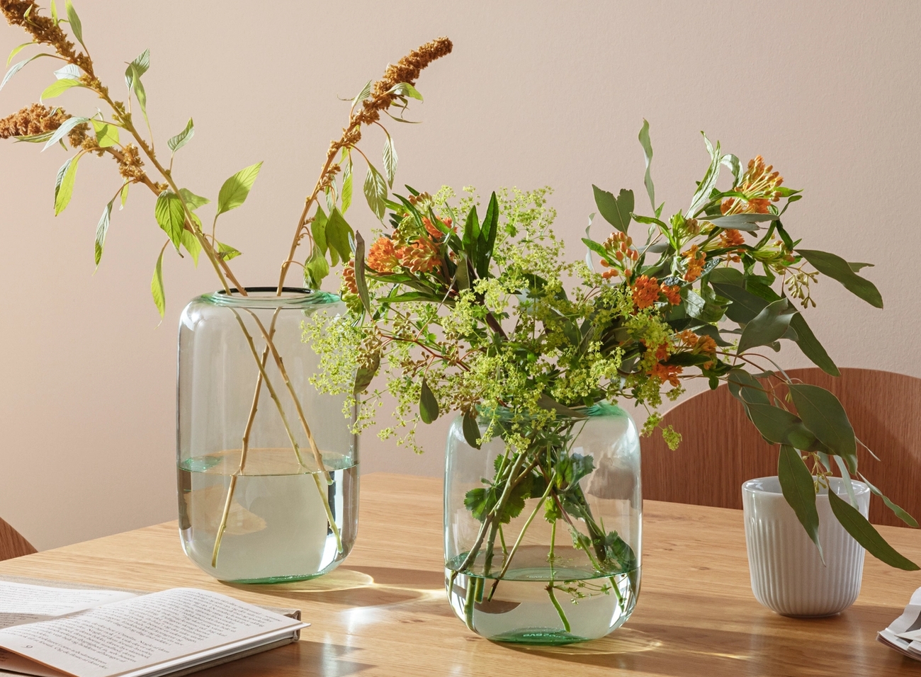 eva solo maljakko valmistettu lasista sävyssä vihreä ruokapöydällä kukkien kirjojen ja lehtien kera