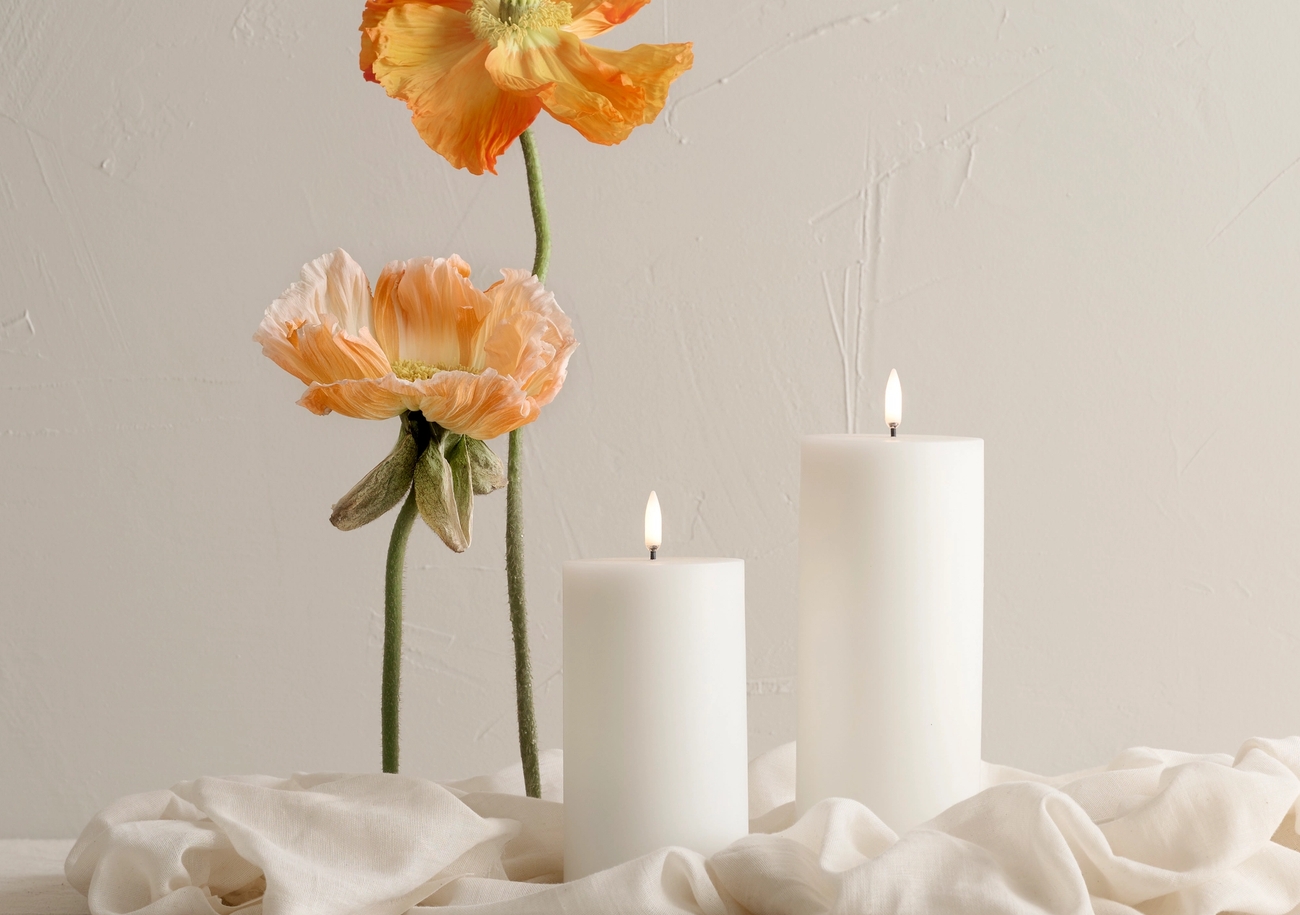 Kynttilät valkoisella liinalla aprikoosin väristen kukkien kera