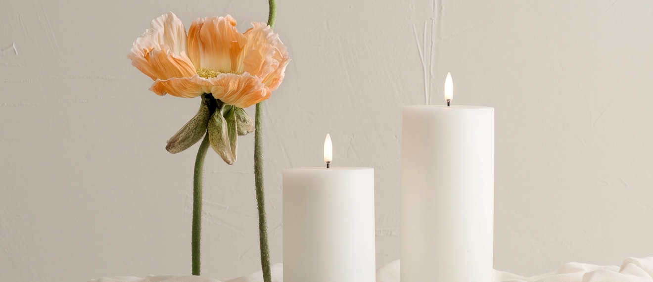 Kynttilät valkoisella liinalla aprikoosin väristen kukkien kera