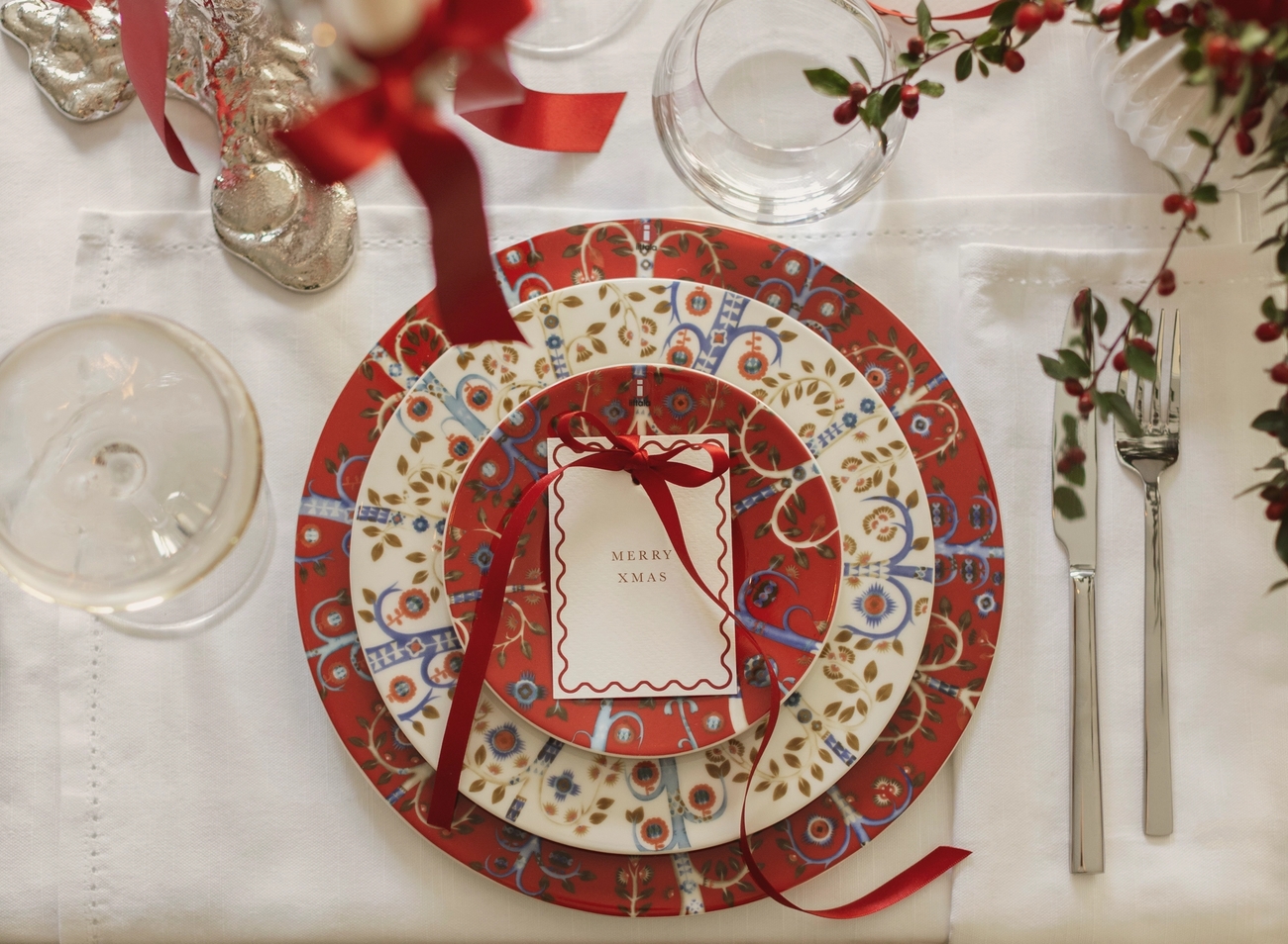 Festlig juleborddekking med mønstrede røde, hvite og blå tallerkener, en GOD JUL-lapp og røde bær.