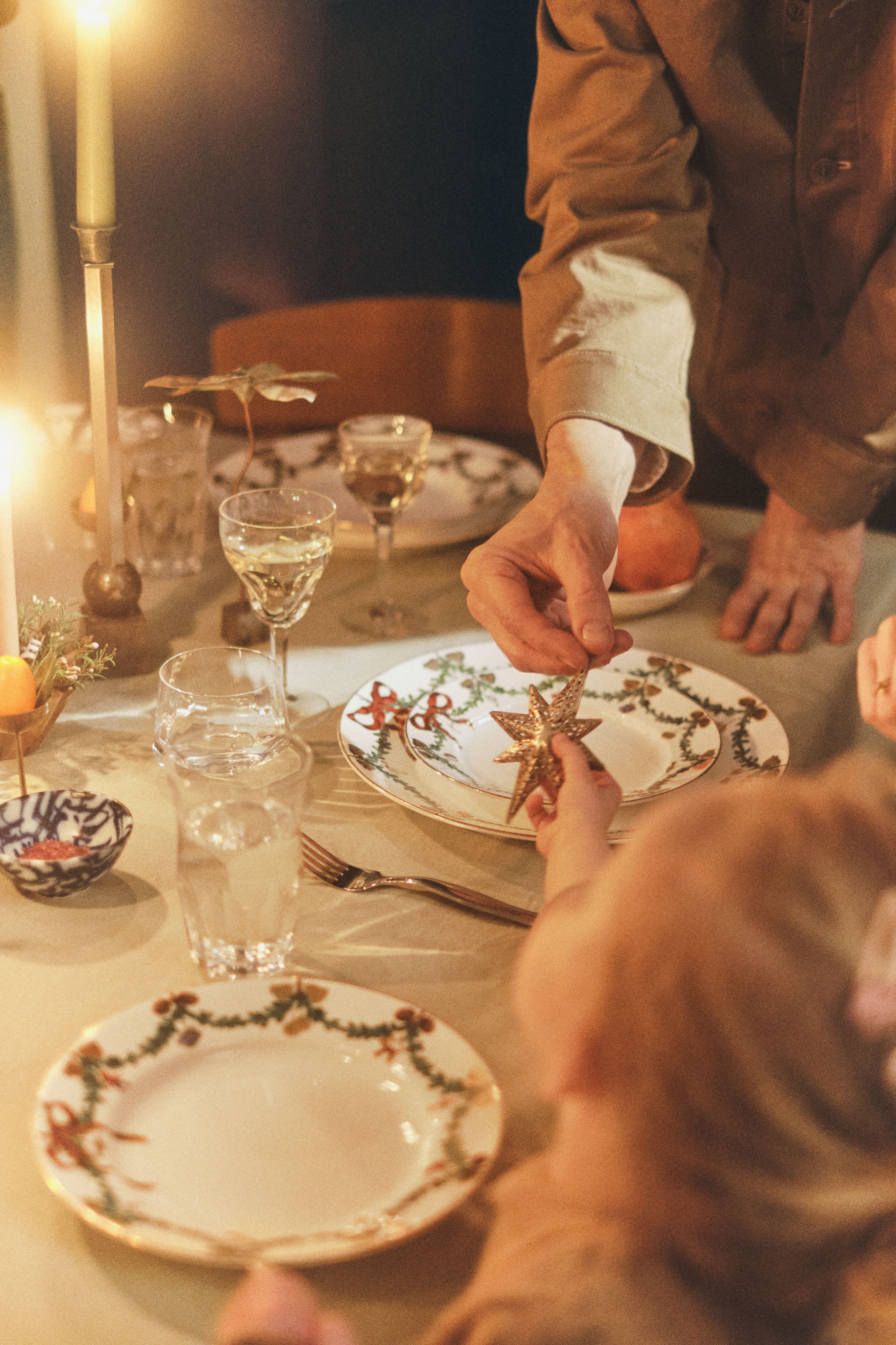 Voksne og barnehender som holder en gyllen stjernepynt ved et festlig middagsbord med levende lys.