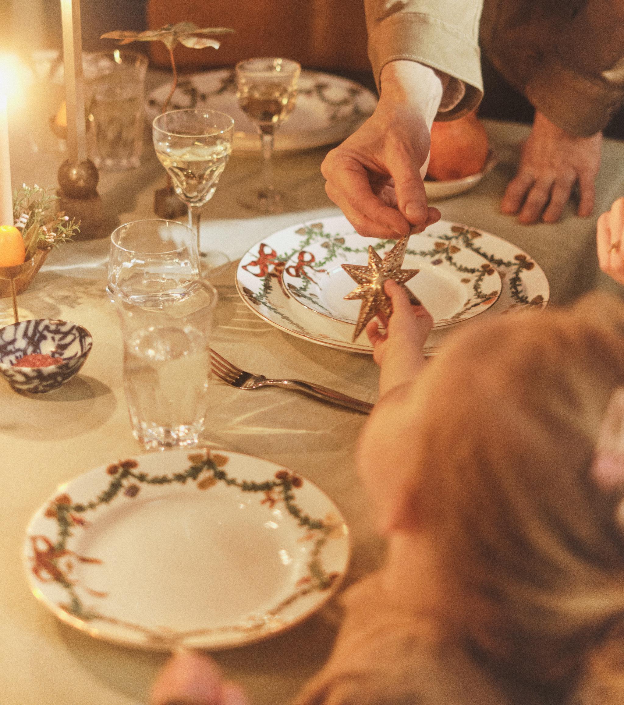 Voksne og barnehender som holder en gyllen stjernepynt ved et festlig middagsbord med levende lys.
