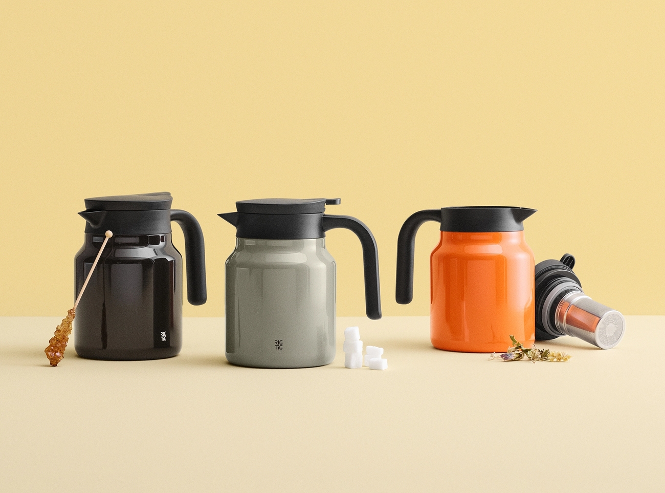 Tre mörkbruna, grå och orange karaffer med svarta lock och handtag, presenterade med socker och tetillbehör.