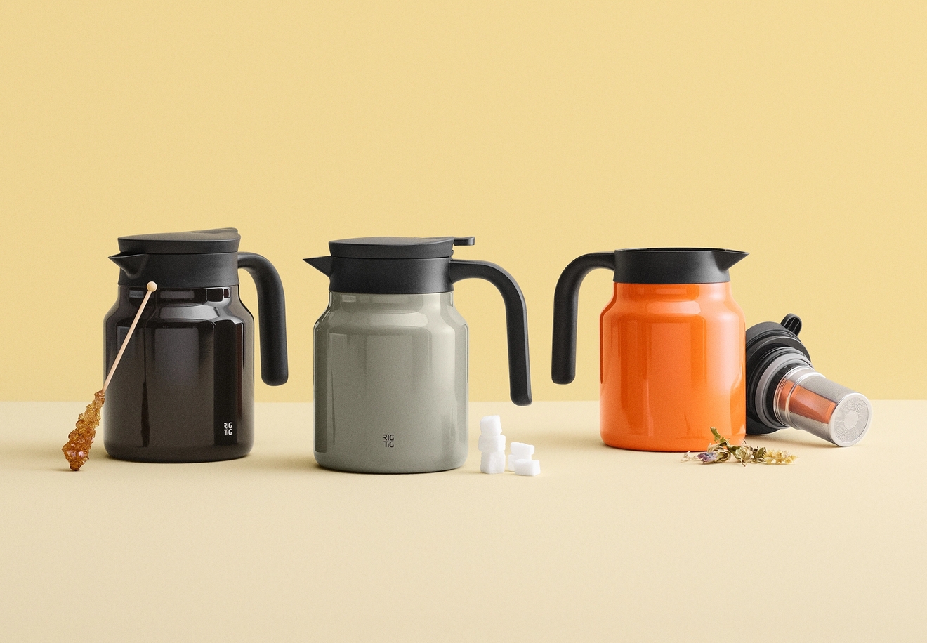 Tre mörkbruna, grå och orange karaffer med svarta lock och handtag, presenterade med socker och tetillbehör.