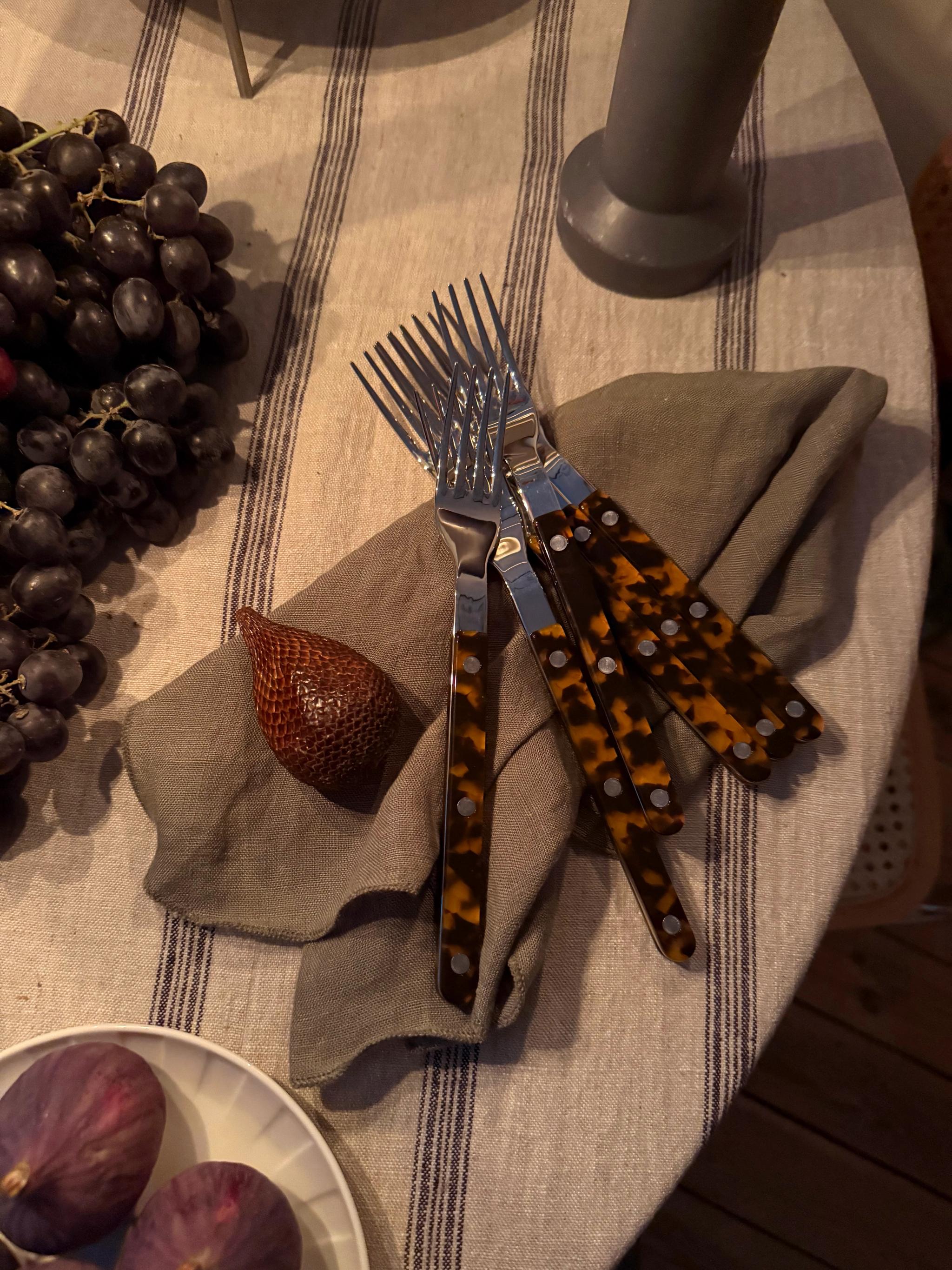 Forks with tortoiseshell handles, grapes, figs, and a snake fruit on a striped tablecloth.