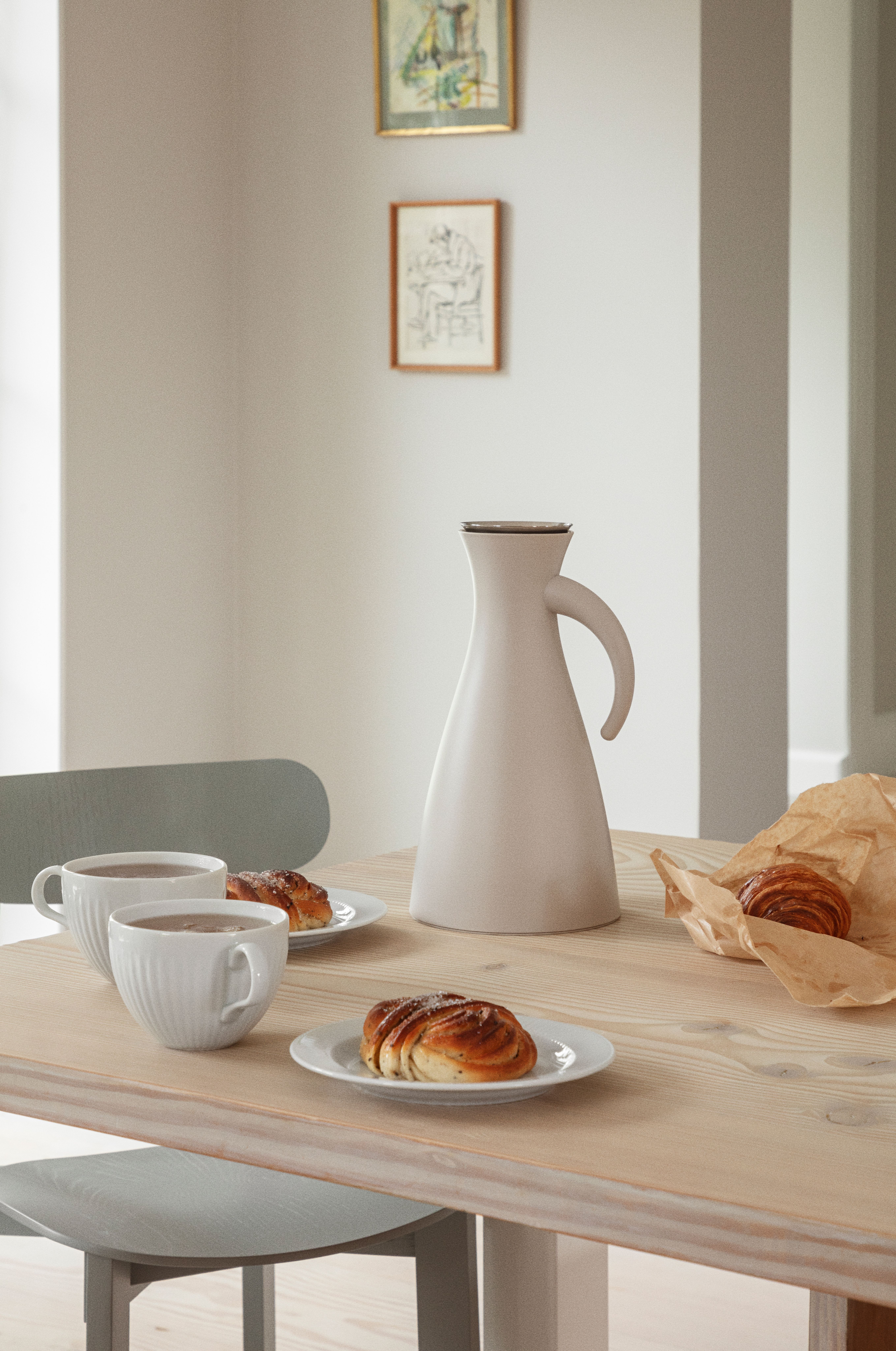 Lyst, minimalistisk frokostbord med hvit termokanne, to kaffekopper og nybakte kanelboller på tallerkener.