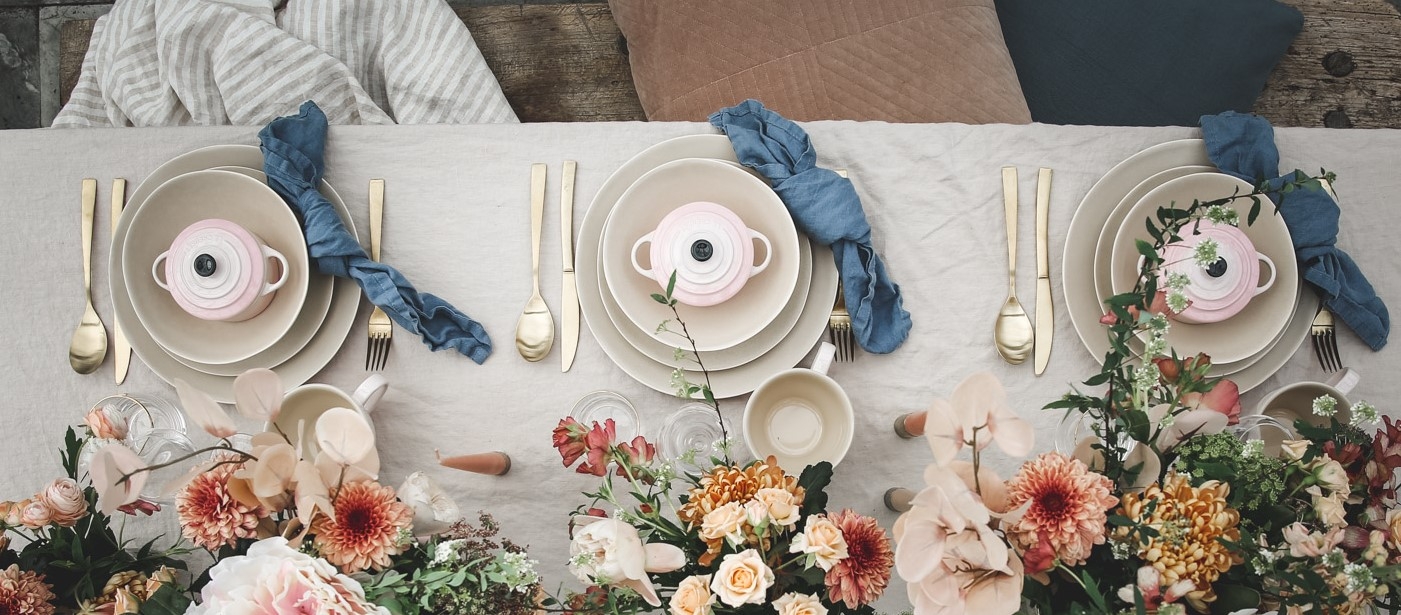Minigrytor Le Creuset i ljusrosa uppdukade på tallrikar med guldiga bestick och blommor