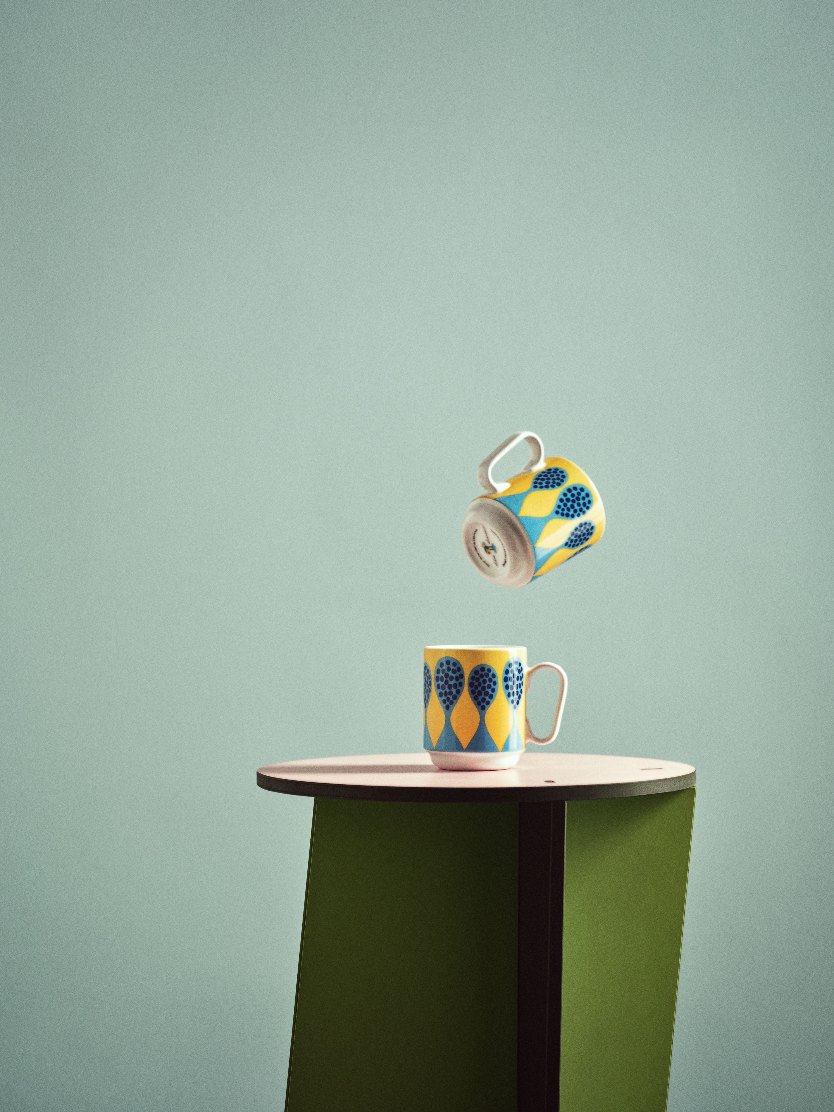 Två mönstrade muggar i gult och blått på en grön pidestal mot en turkos bakgrund