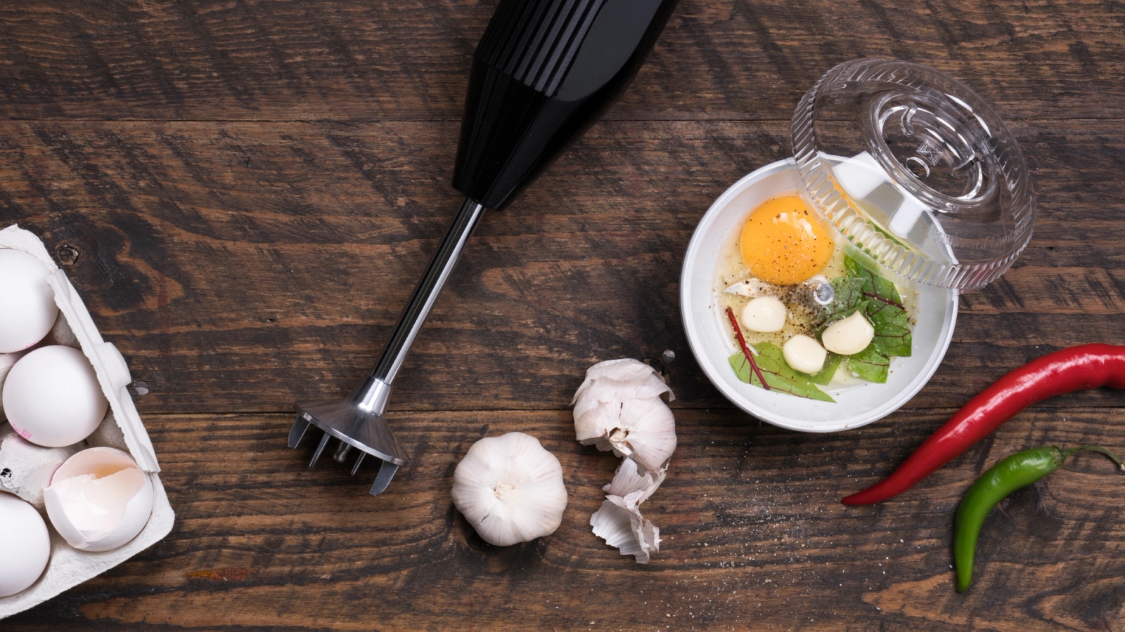 Stavmixer på träbord med vitlök, ägg och chili