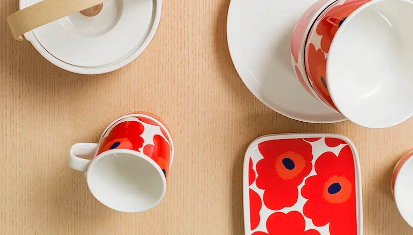 Pöydällä on Marimekon Unikko-kuvioituja punavalkoisia astioita, kuten mukeja, lautanen ja teekannu.