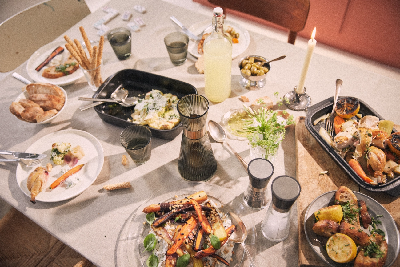 A rustic dining table covered in various dishes from a partially eaten meal, including roasted chicken, carrots, and bread.