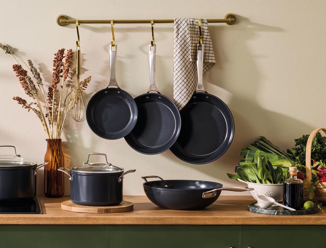 Tyylikäs kokoelma tummanharmaita kattiloita ja pannuja keittiössä.