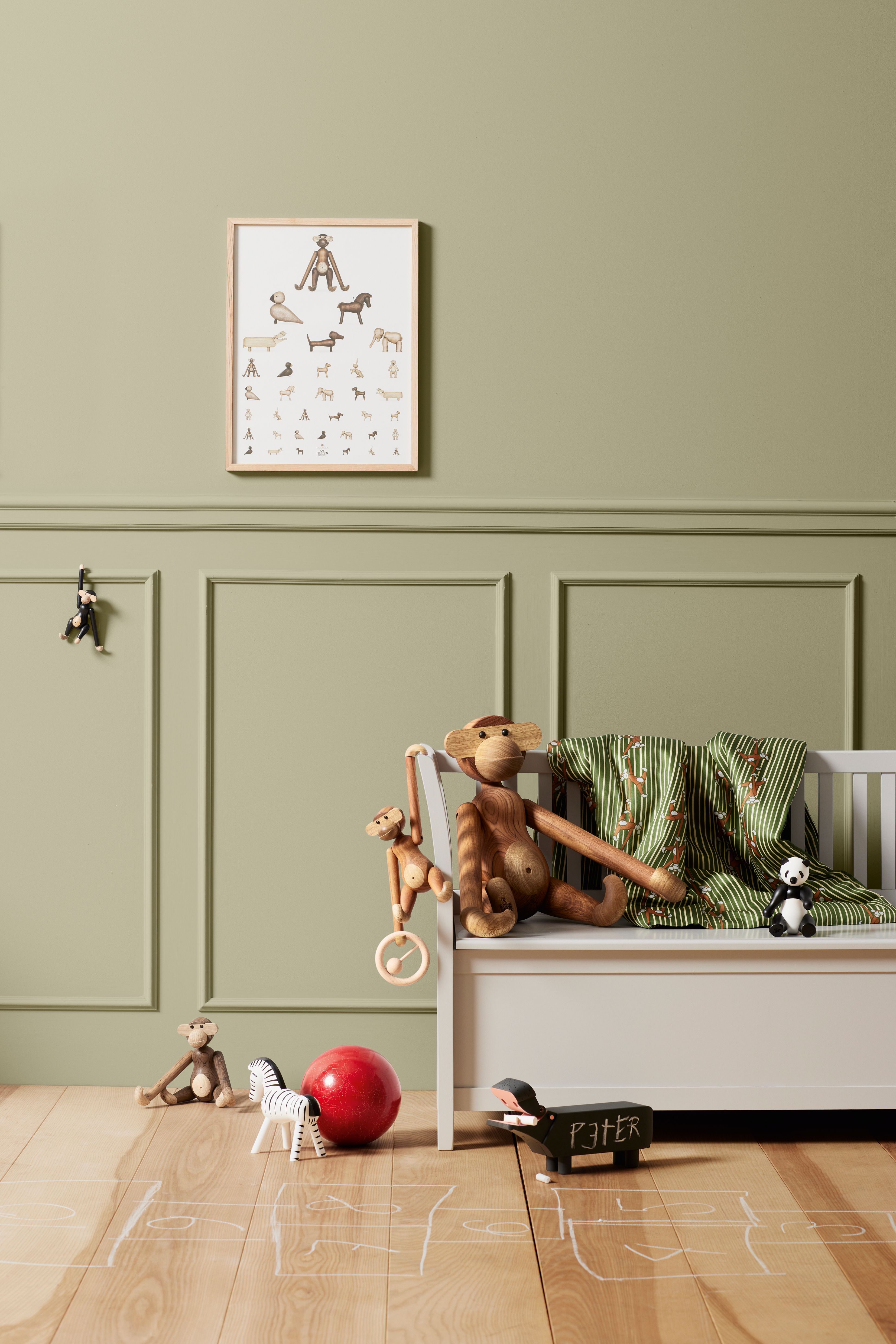 A playful child's room with sage green wainscoting, an animal poster, a bench holding wooden monkey toys and a green blanket, and toys on a chalk-drawn wooden floor.