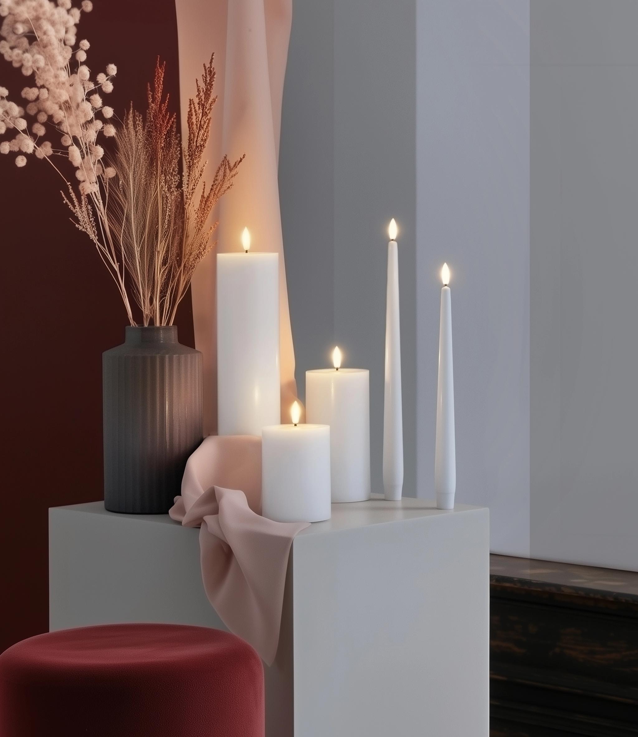 En grupp vita ljus står på ett bord bredvid en vas med torkade blommor.
