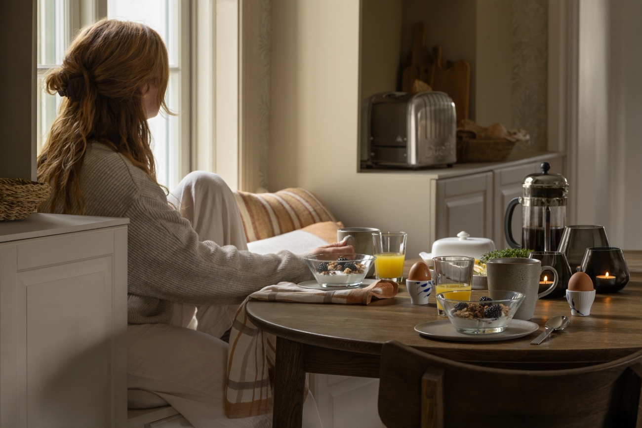 En kvinna sitter vid ett bord och äter frukost och läser en bok.