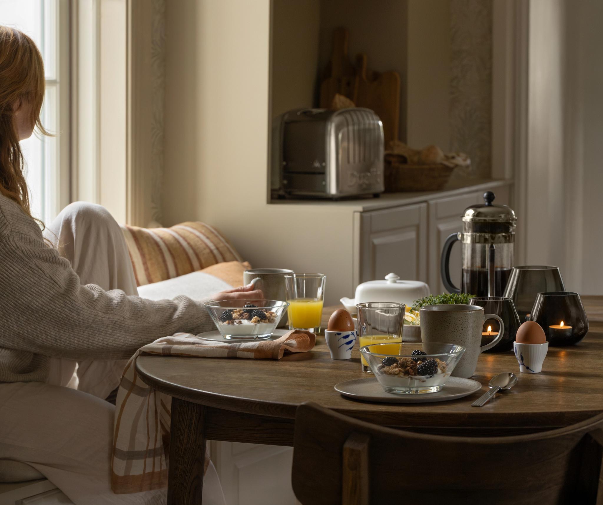 En kvinne sitter ved et bord og spiser frokost mens hun leser en bok