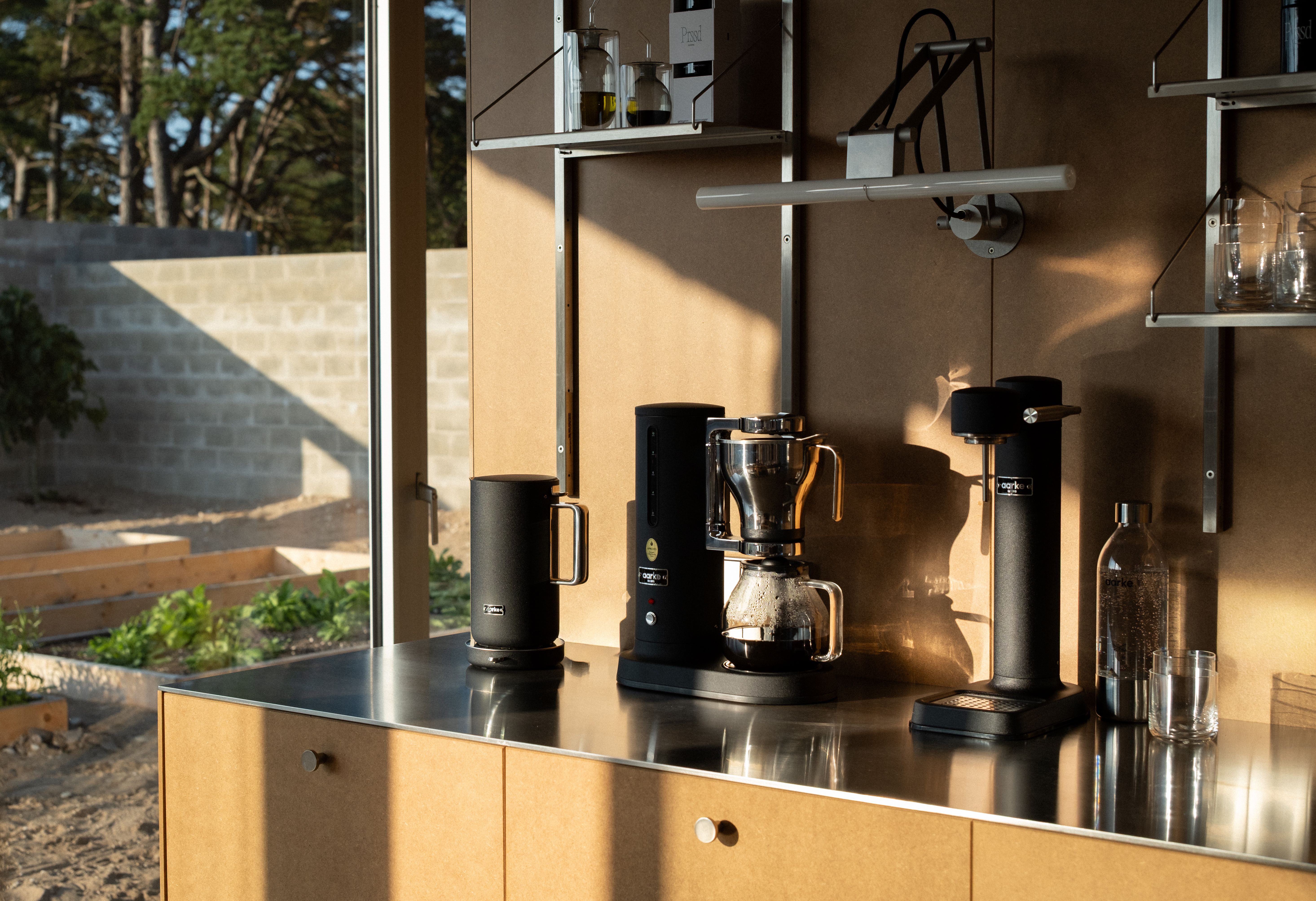 Svart kaffemaskin och svart vattenkokare från Aarke på en modern köksbänk med solig trädgårdsutsikt.