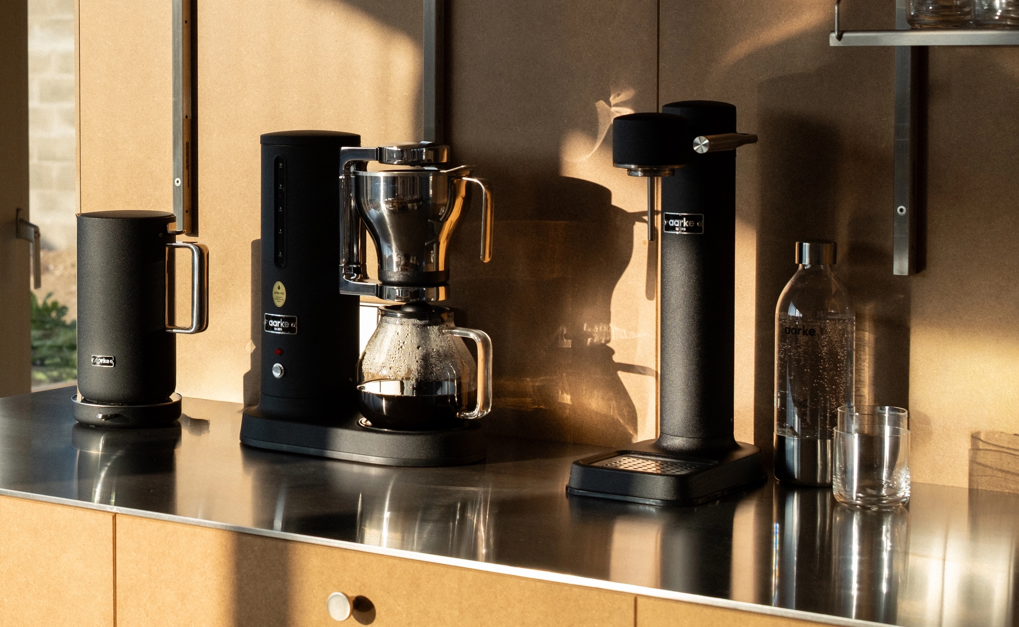 Svart kaffemaskin och svart vattenkokare från Aarke på en modern köksbänk med solig trädgårdsutsikt.