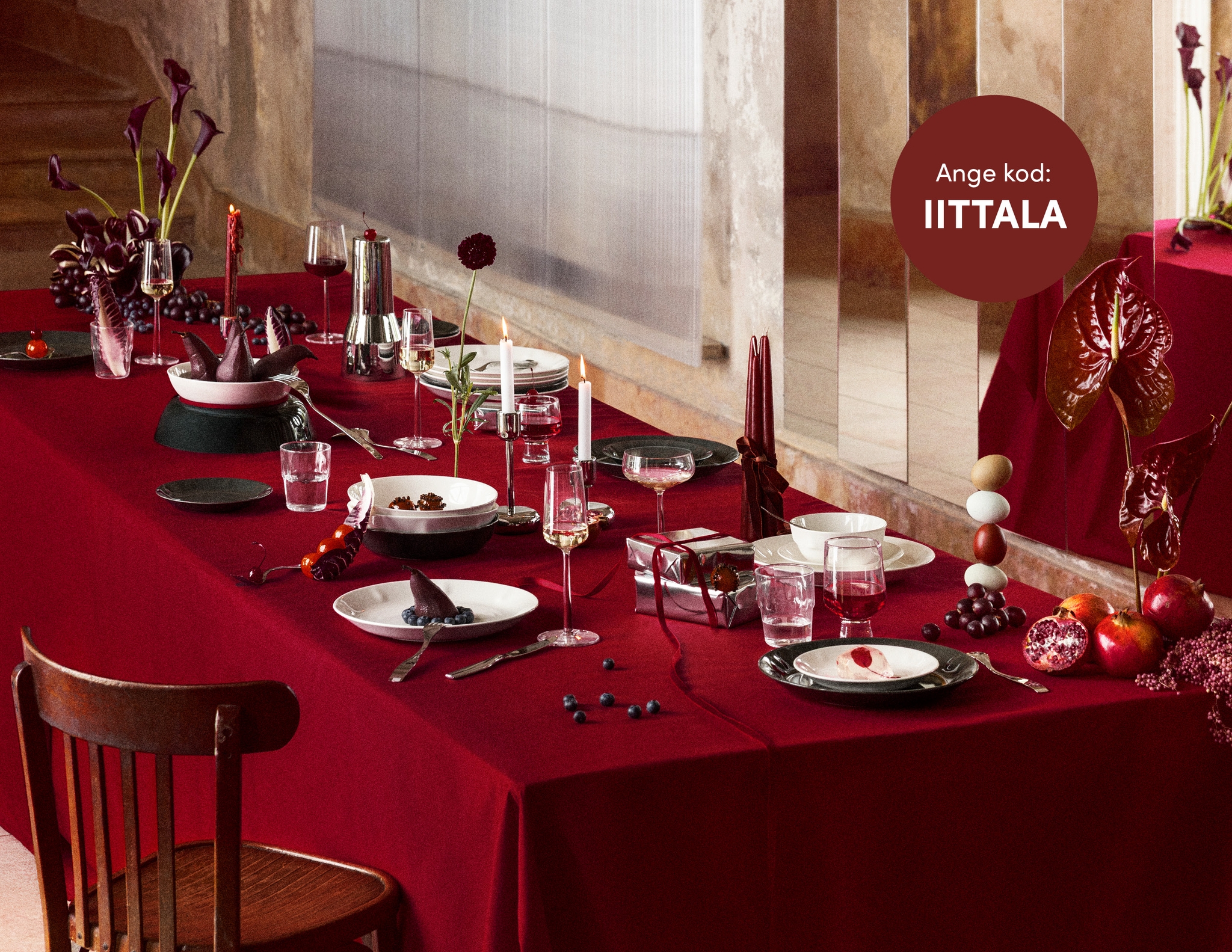  Ett långt matbord dukat med elegant vitt porslin, glas, mörkröda ljus och blommor på en djupröd duk.