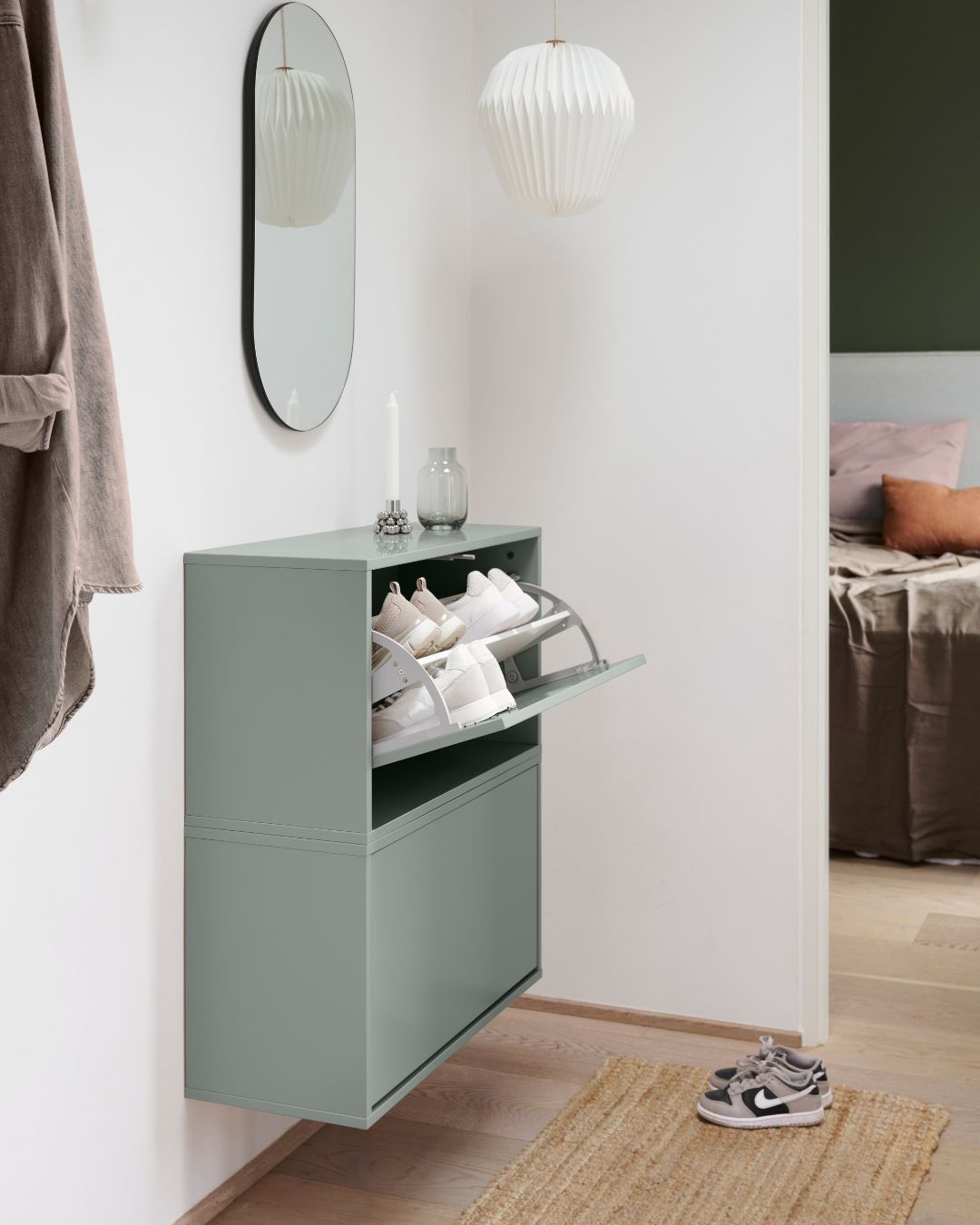 Modern hall med väggmonterat grönt skoskåp, spegel och stilren belysning.