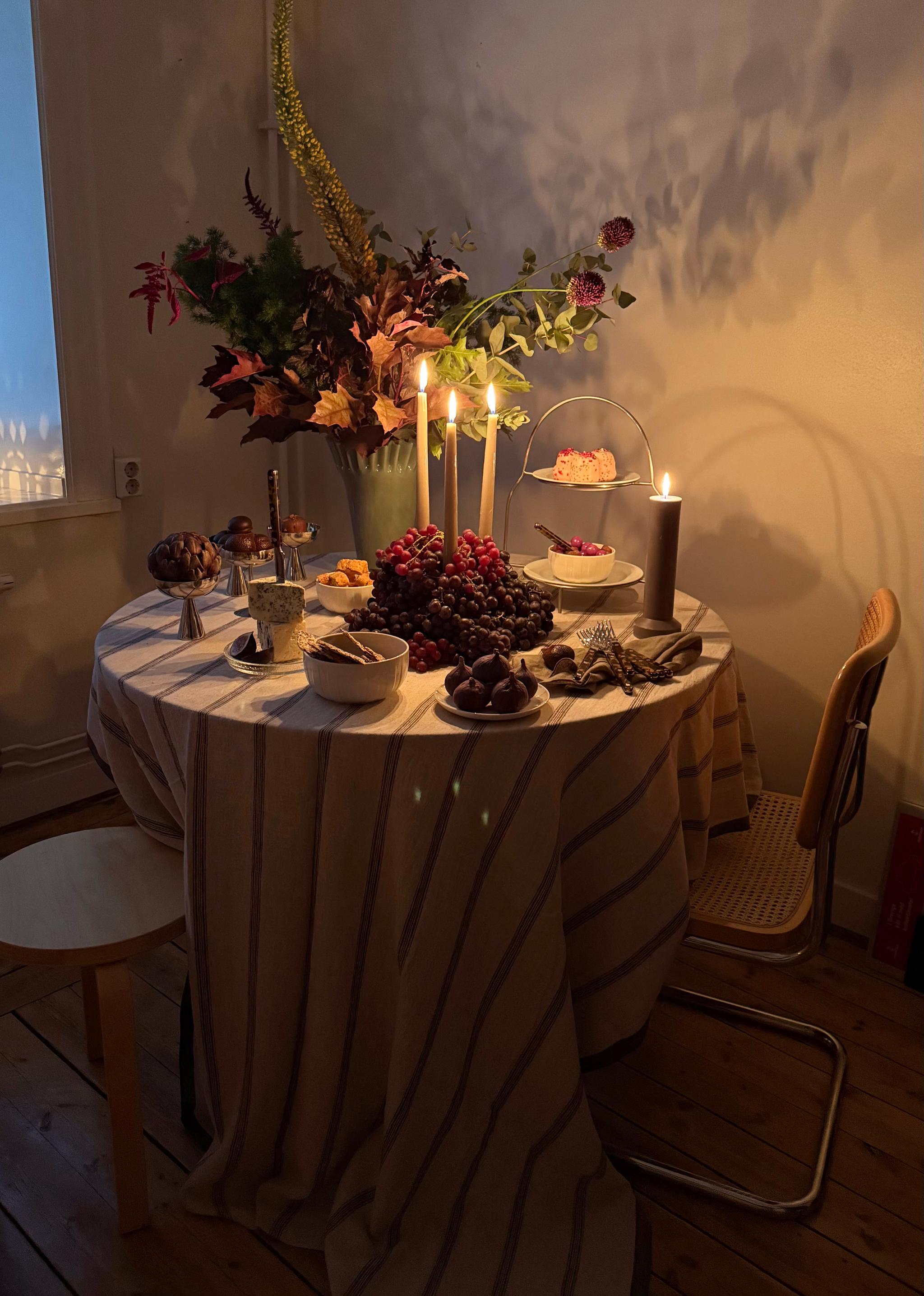 A candlelit table set with a large autumn floral arrangement, abundant grapes, figs, desserts, and snacks.