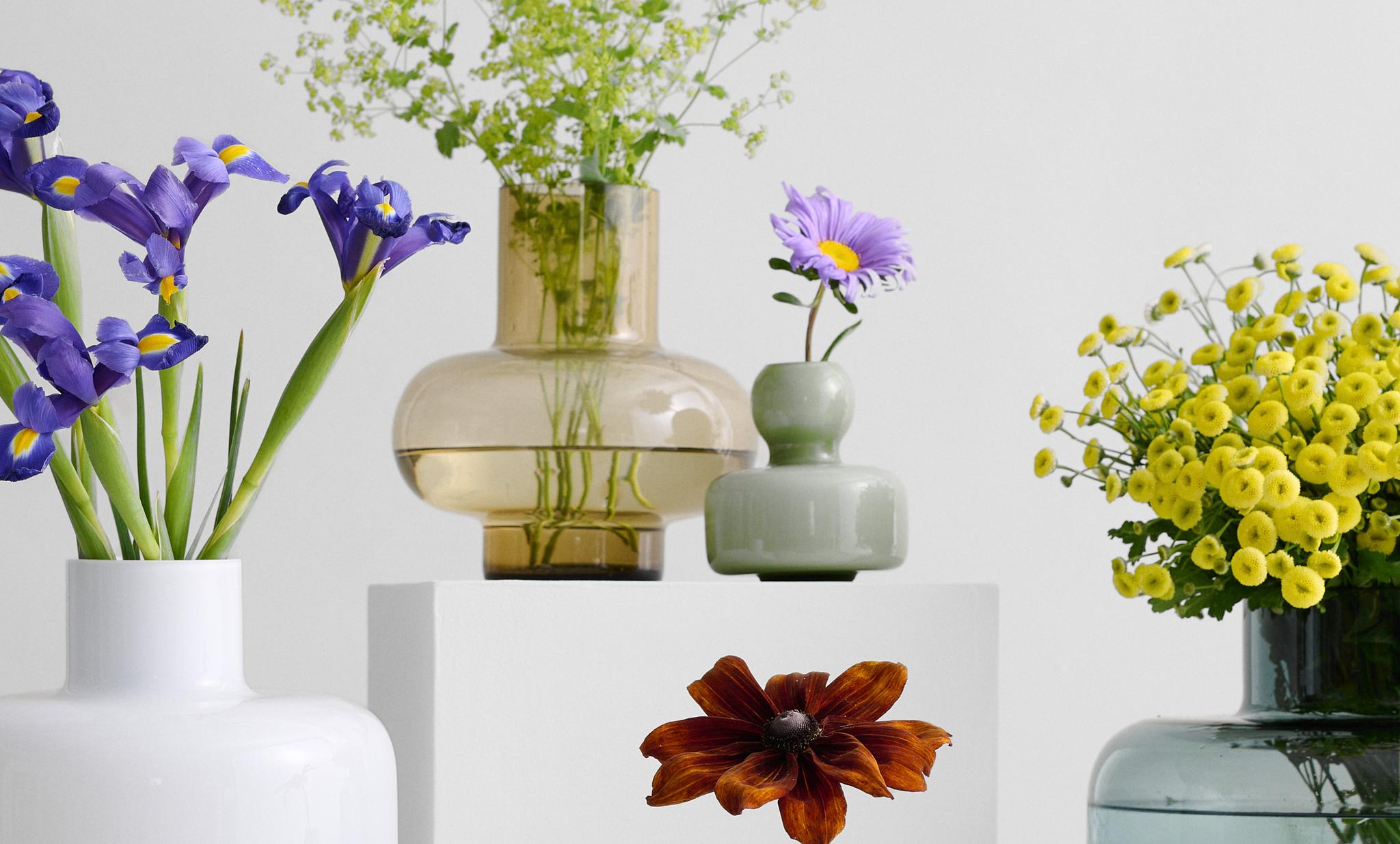 Värikkäät kukat eri muotoisissa design-maljakoissa valkoisella tasolla modernia sisustusta vasten.