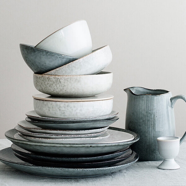 Stengods tallrikar travade på varann i färgerna grått, vitt och grönt